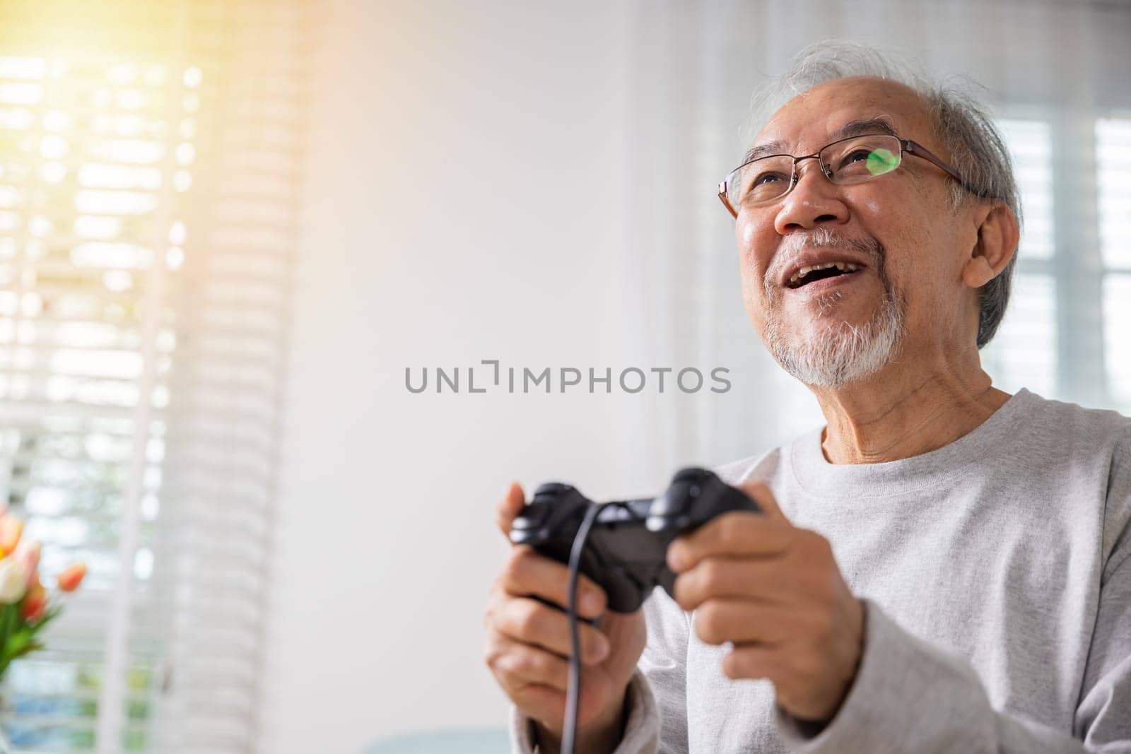 Asian mature man hands using game controller play videogame, Funny on retirement elderly smile sitting on sofa life gaming, senior old man enjoying holding joystick playing video game at home