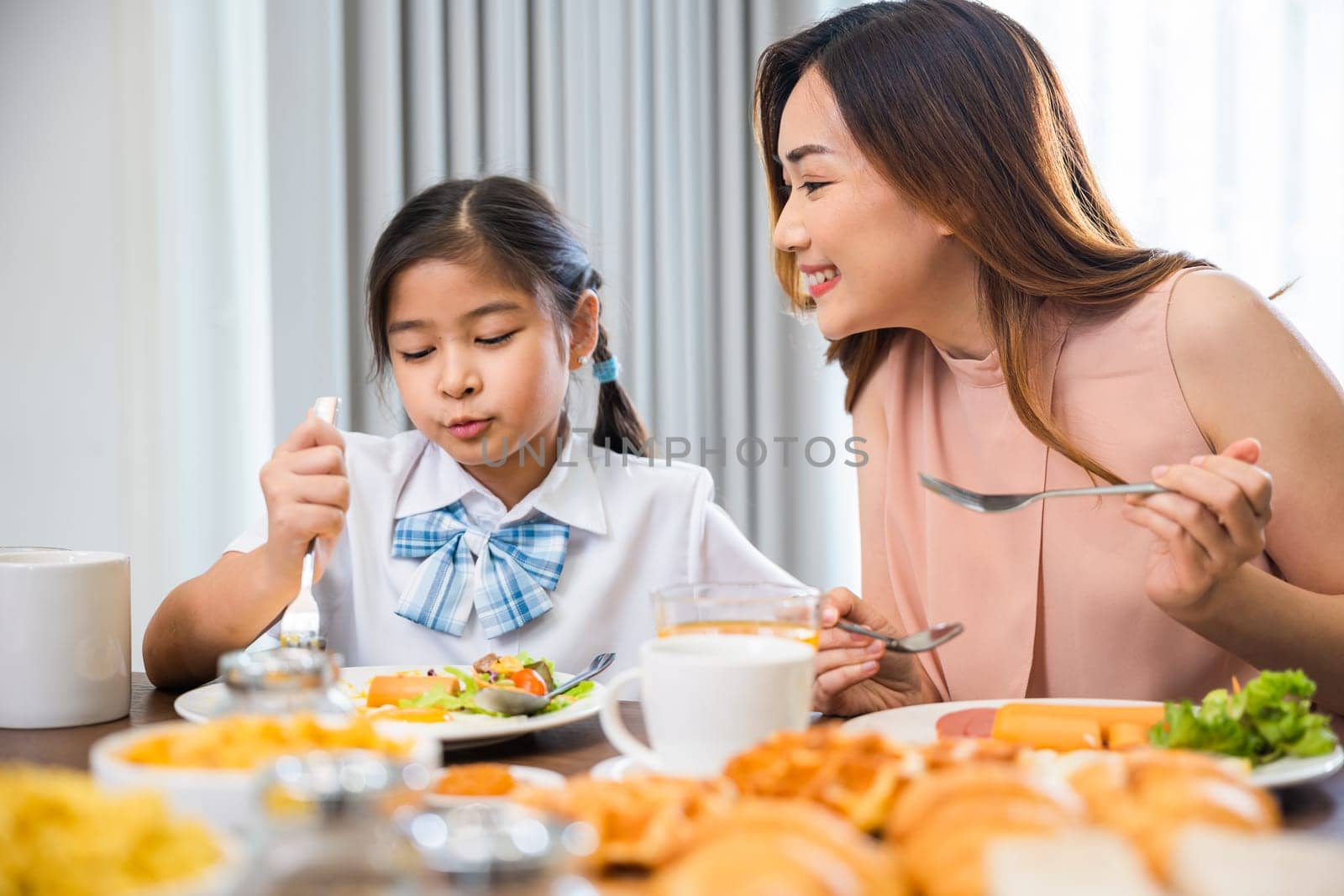 Family breakfast. Mom and little preschooler have fun smile eating meal together, Asian mother and child daughter having breakfast on food table, Healthy food at home in morning before go to school