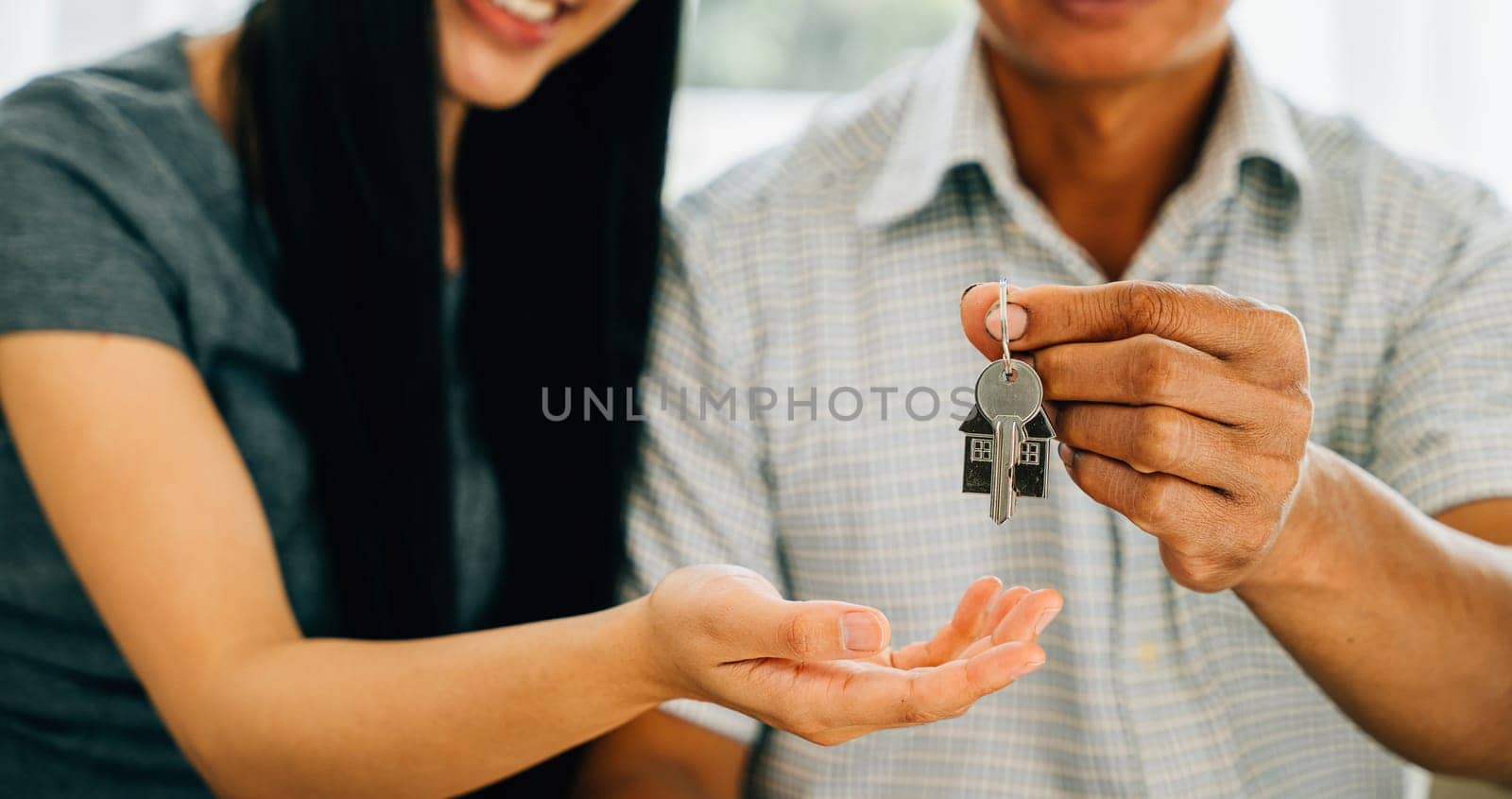 A delighted couple celebrates new homeownership displaying keys to their house by Sorapop