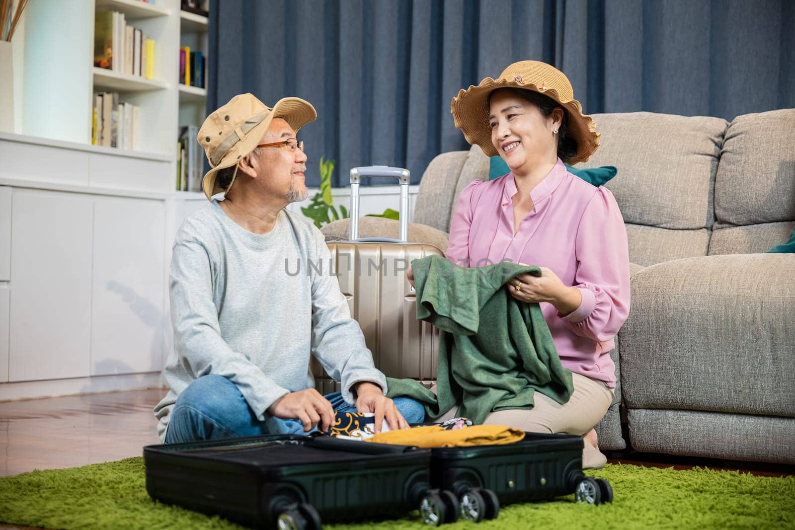 Asian romantic retired couple packing clothes travel bag suitcase together on floor at home by Sorapop