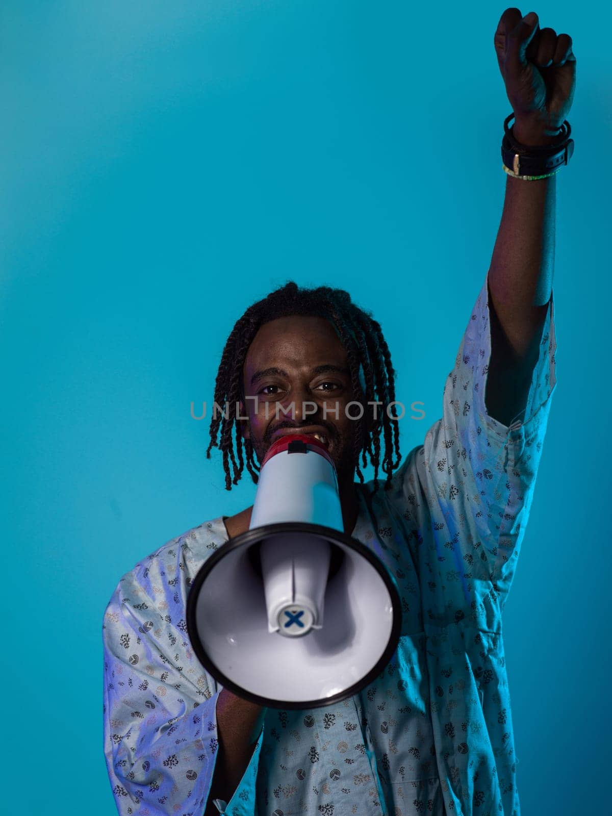 In a powerful and symbolic image, an African American man wears traditional clothing, passionately wields a megaphone against a striking blue background, with his hand raised in the air symbolizing his vocal and cultural empowerment in the pursuit of social justice and equality by dotshock