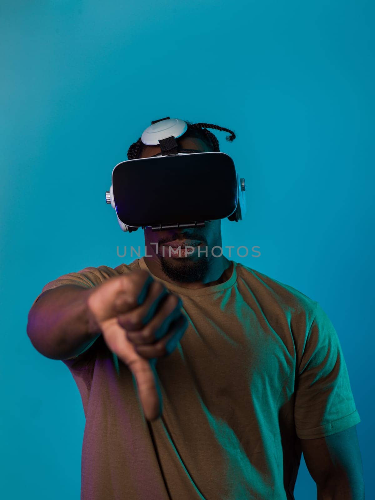 African American man, wearing virtual reality glasses, expresses dissatisfaction by pointing down with his hand while standing isolated against a blue background, portraying a modern critique within the immersive digital realm by dotshock
