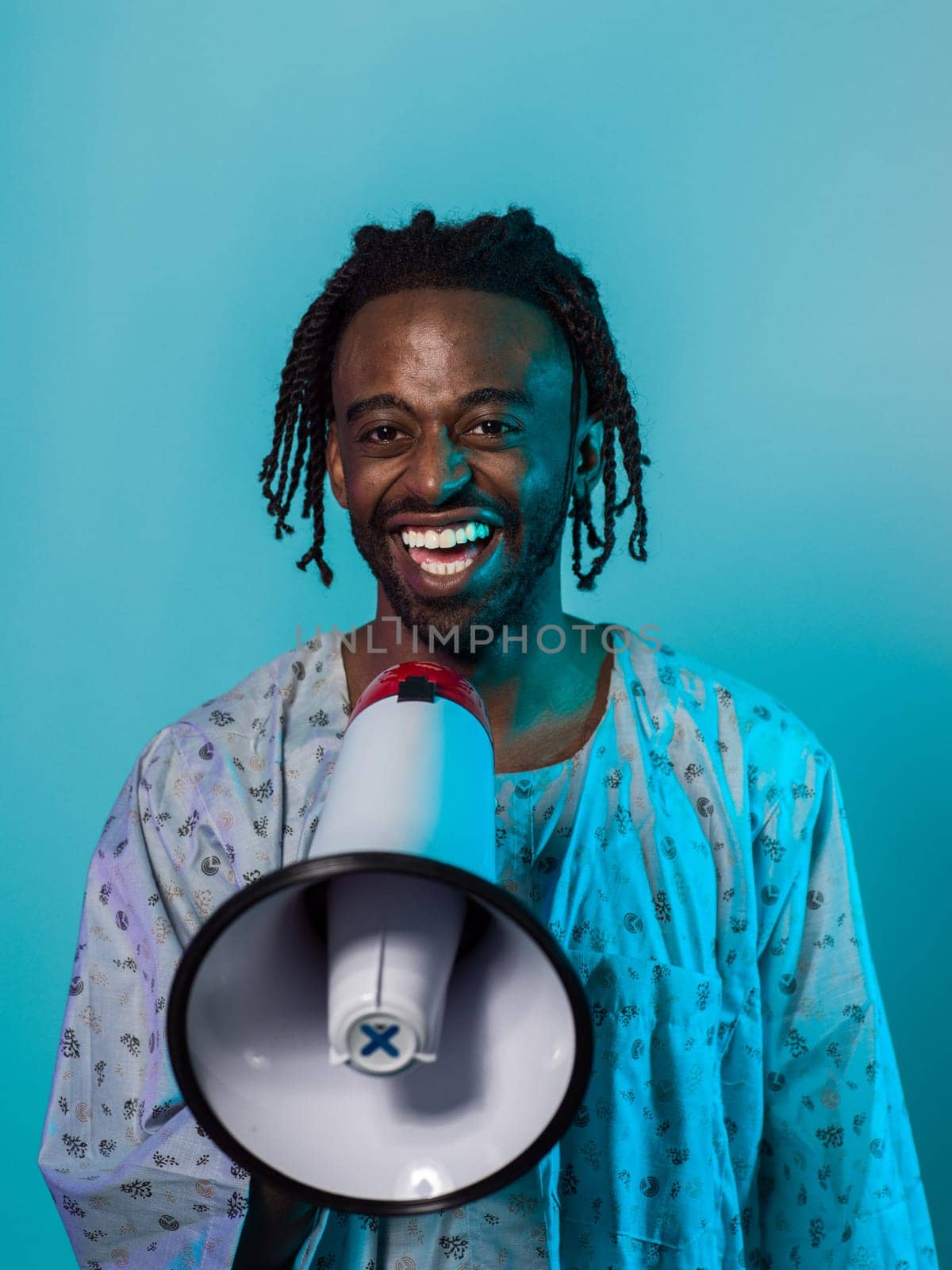 African American man dons traditional attire, passionately utilizing a megaphone against a striking blue background, symbolizing his vocal and cultural empowerment in the pursuit of social justice and equality by dotshock