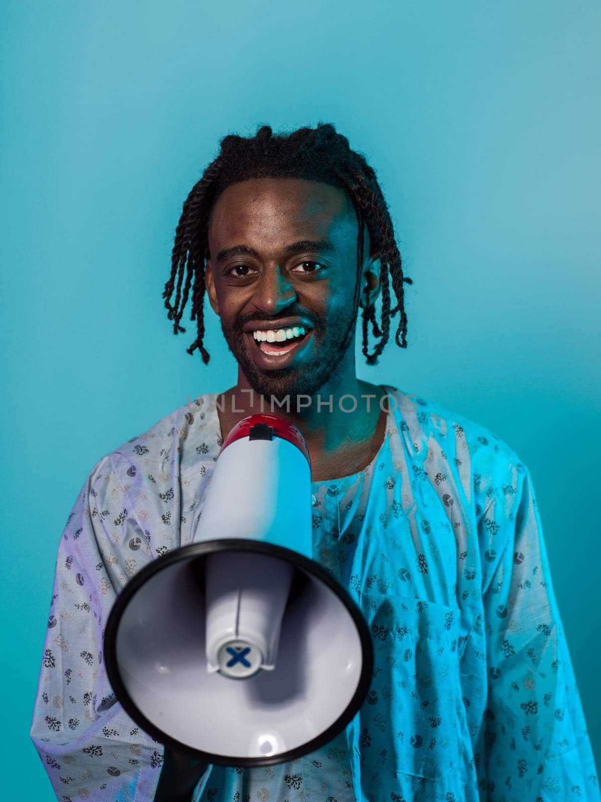 African American man dons traditional attire, passionately utilizing a megaphone against a striking blue background, symbolizing his vocal and cultural empowerment in the pursuit of social justice and equality by dotshock