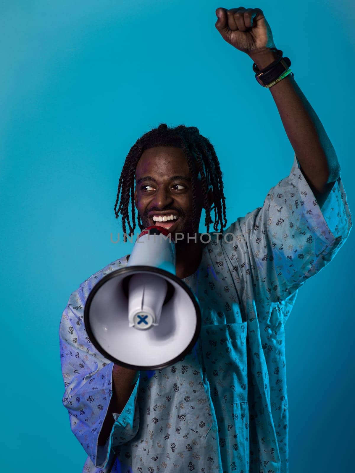 In a powerful and symbolic image, an African American man wears traditional clothing, passionately wields a megaphone against a striking blue background, with his hand raised in the air symbolizing his vocal and cultural empowerment in the pursuit of social justice and equality by dotshock