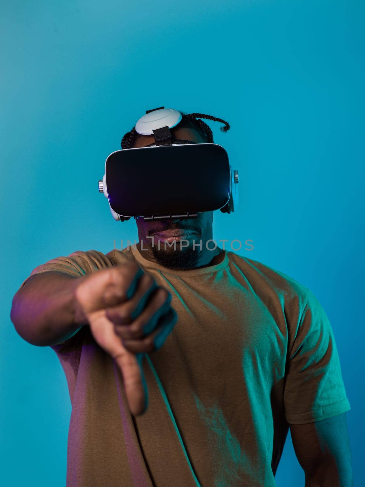 African American man, wearing virtual reality glasses, expresses dissatisfaction by pointing down with his hand while standing isolated against a blue background, portraying a modern critique within the immersive digital realm.