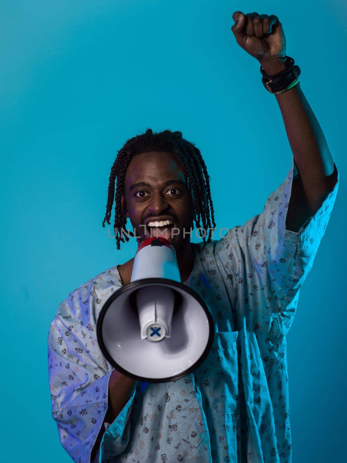 In a powerful and symbolic image, an African American man wears traditional clothing, passionately wields a megaphone against a striking blue background, with his hand raised in the air symbolizing his vocal and cultural empowerment in the pursuit of social justice and equality.