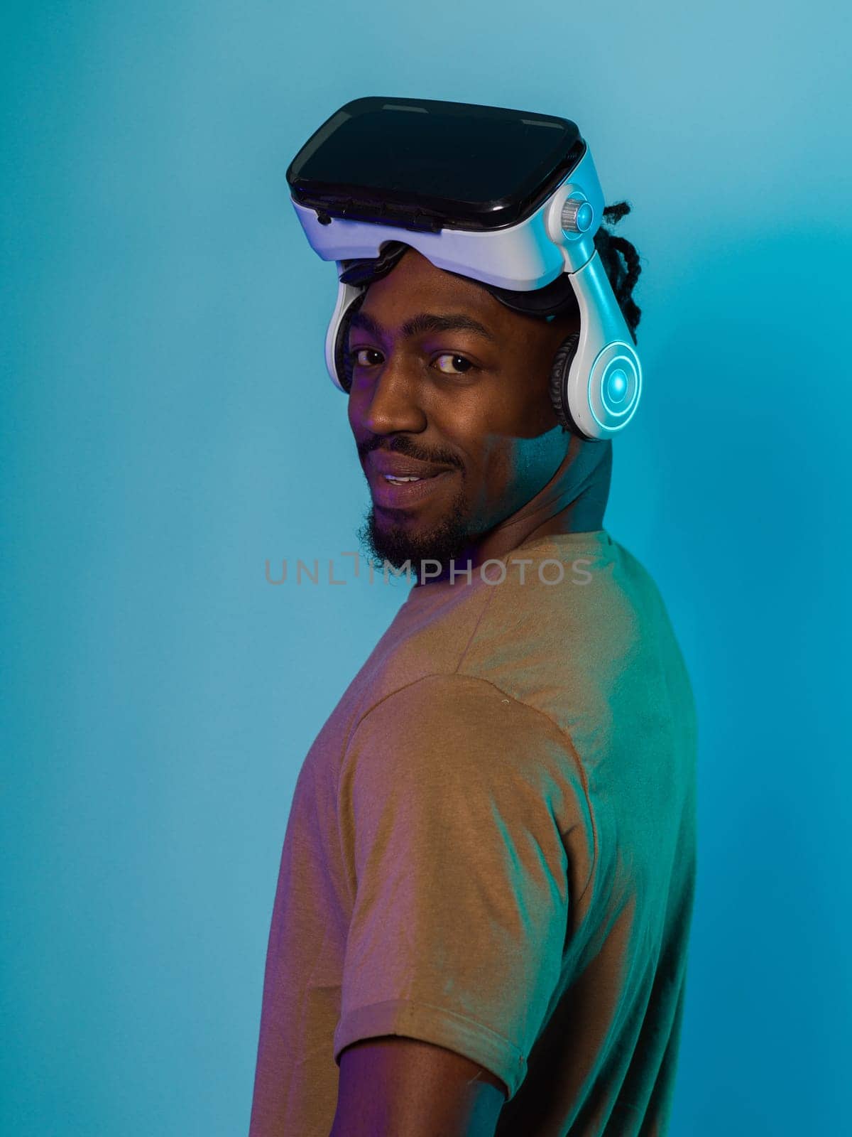 In a futuristic visual, an African American man stands isolated against a striking blue backdrop, adorned with VR glasses that transport him into a cutting-edge virtual reality experience, merging technology and innovation in a contemporary display.