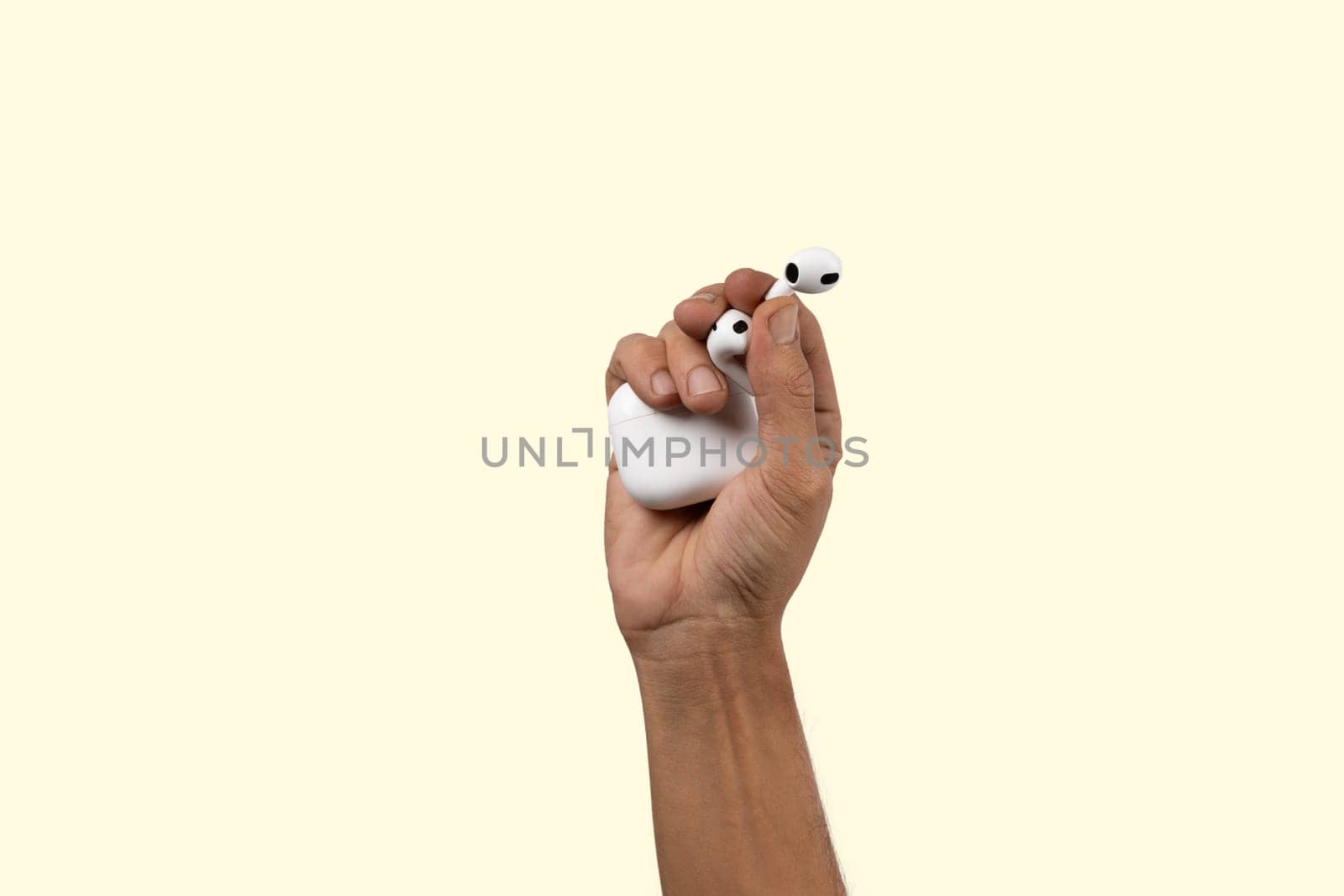 Black male hand holding a pair of earbuds on Light yellow background. by TropicalNinjaStudio