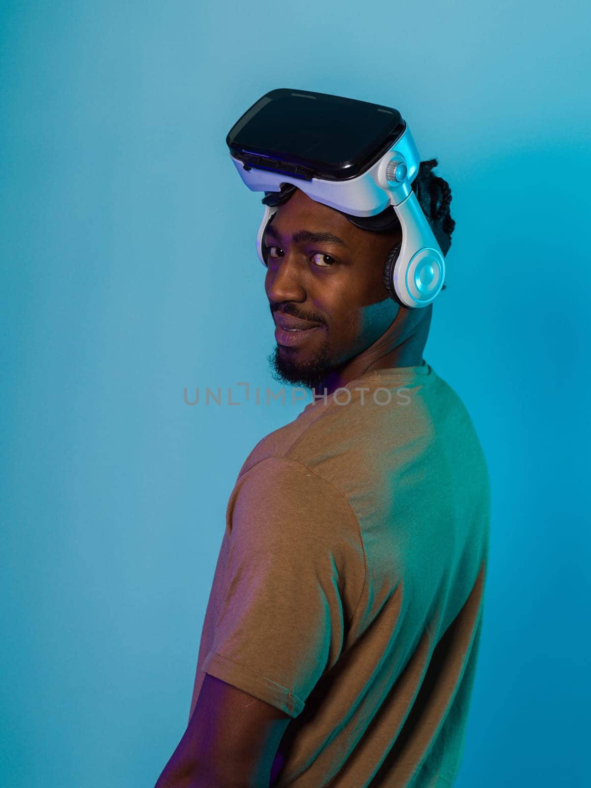 In a futuristic visual, an African American man stands isolated against a striking blue backdrop, adorned with VR glasses that transport him into a cutting-edge virtual reality experience, merging technology and innovation in a contemporary display by dotshock