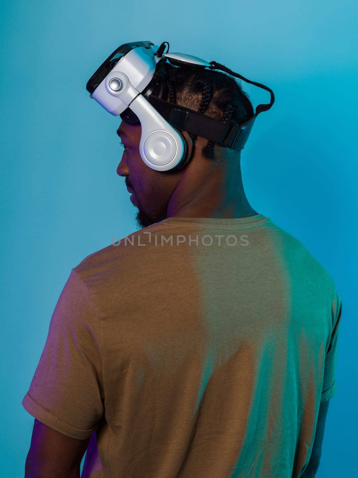 In a futuristic visual, an African American man stands isolated against a striking blue backdrop, adorned with VR glasses that transport him into a cutting-edge virtual reality experience, merging technology and innovation in a contemporary display.