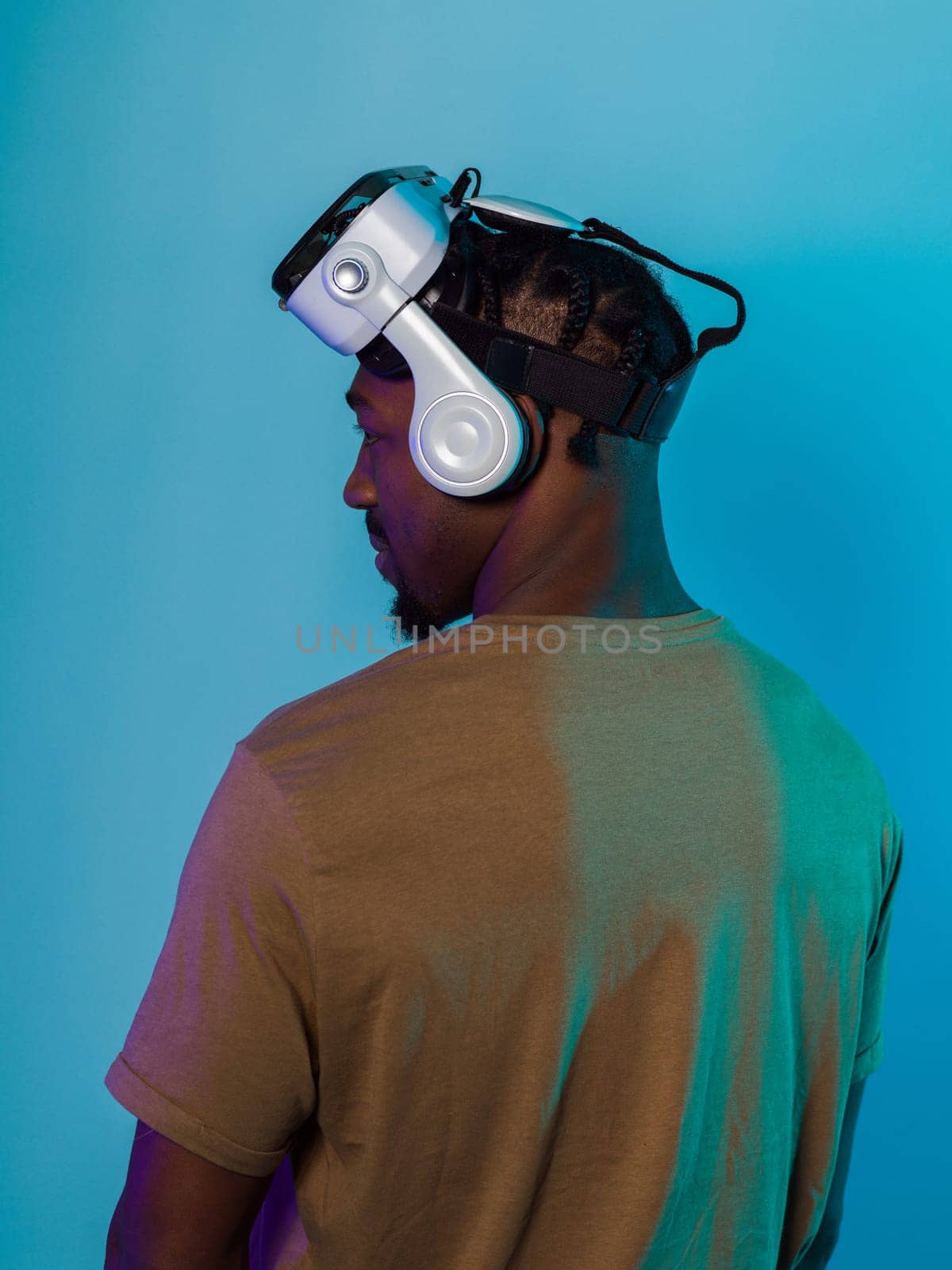 In a futuristic visual, an African American man stands isolated against a striking blue backdrop, adorned with VR glasses that transport him into a cutting-edge virtual reality experience, merging technology and innovation in a contemporary display by dotshock