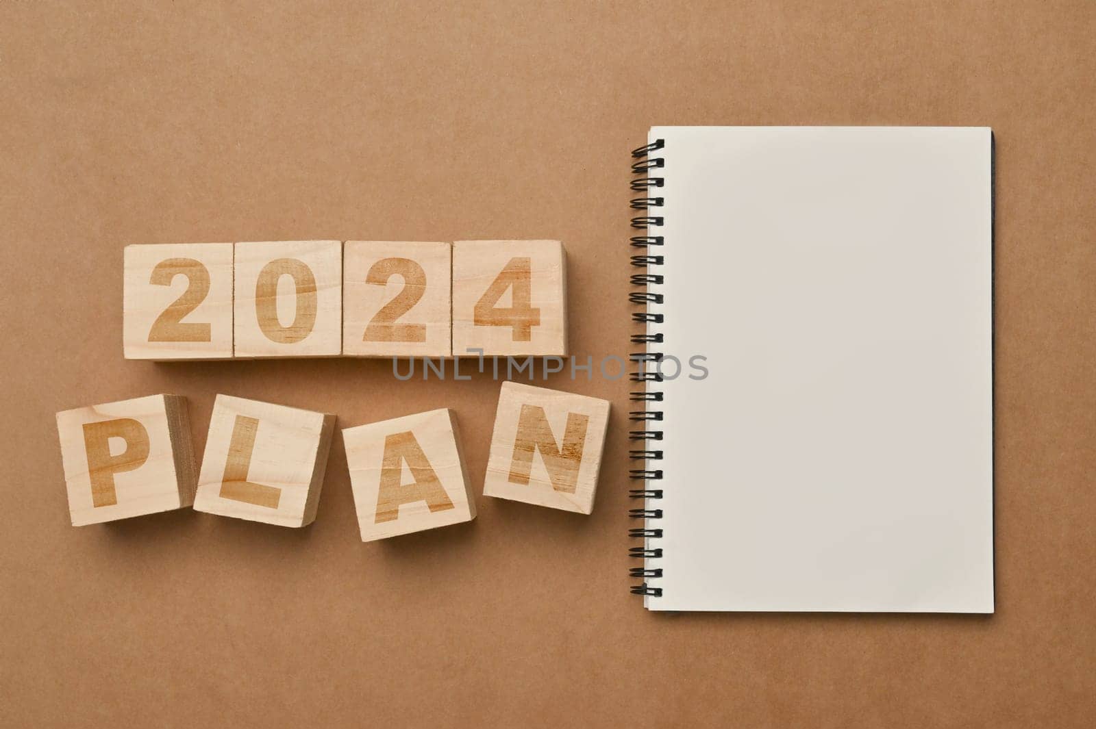 Wooden cubes with 2024 PLAN and notebook on brown background. Business plan, goals and strategy concept by prathanchorruangsak