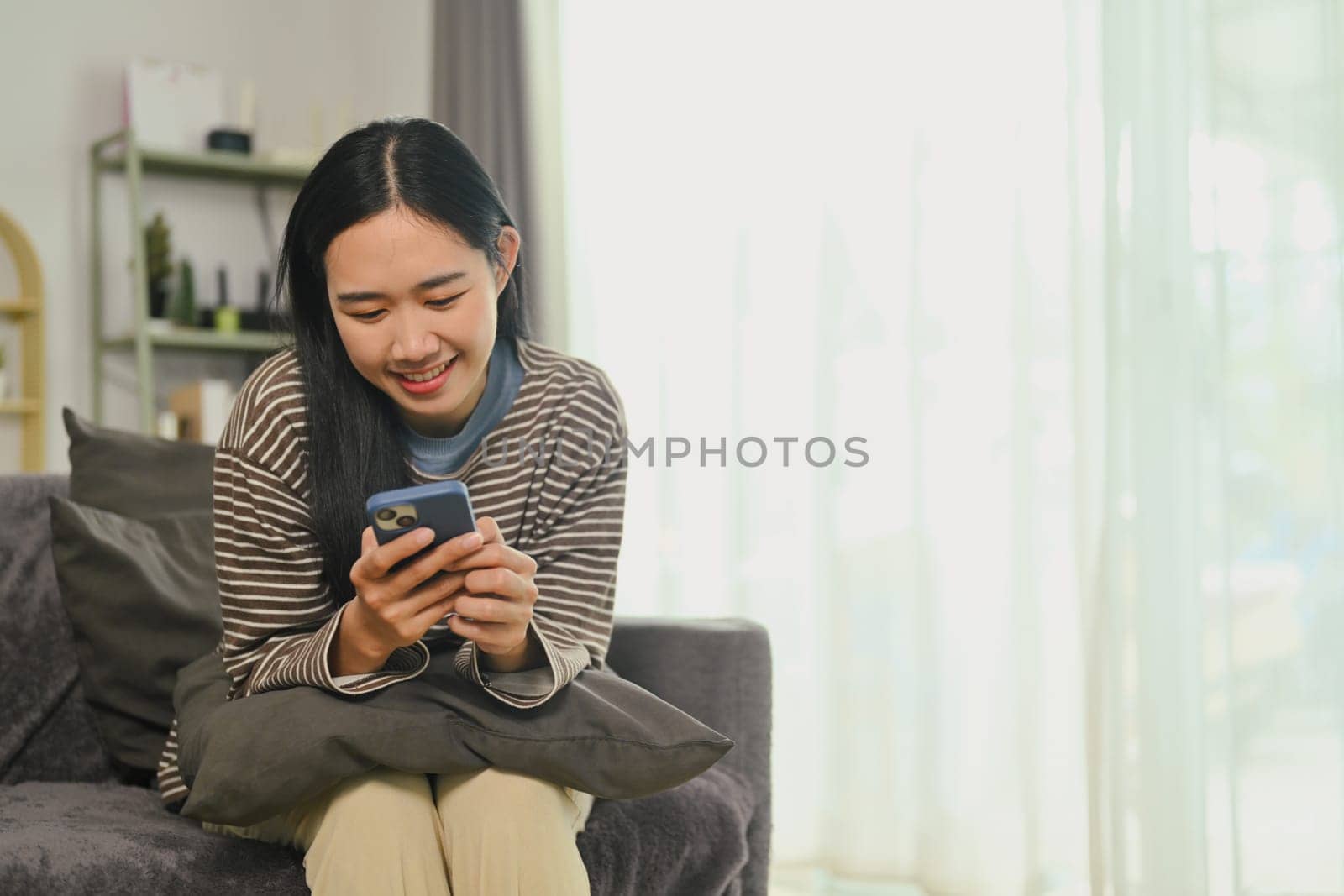 Cheerful young woman checking news and messaging in social network on mobile phone.