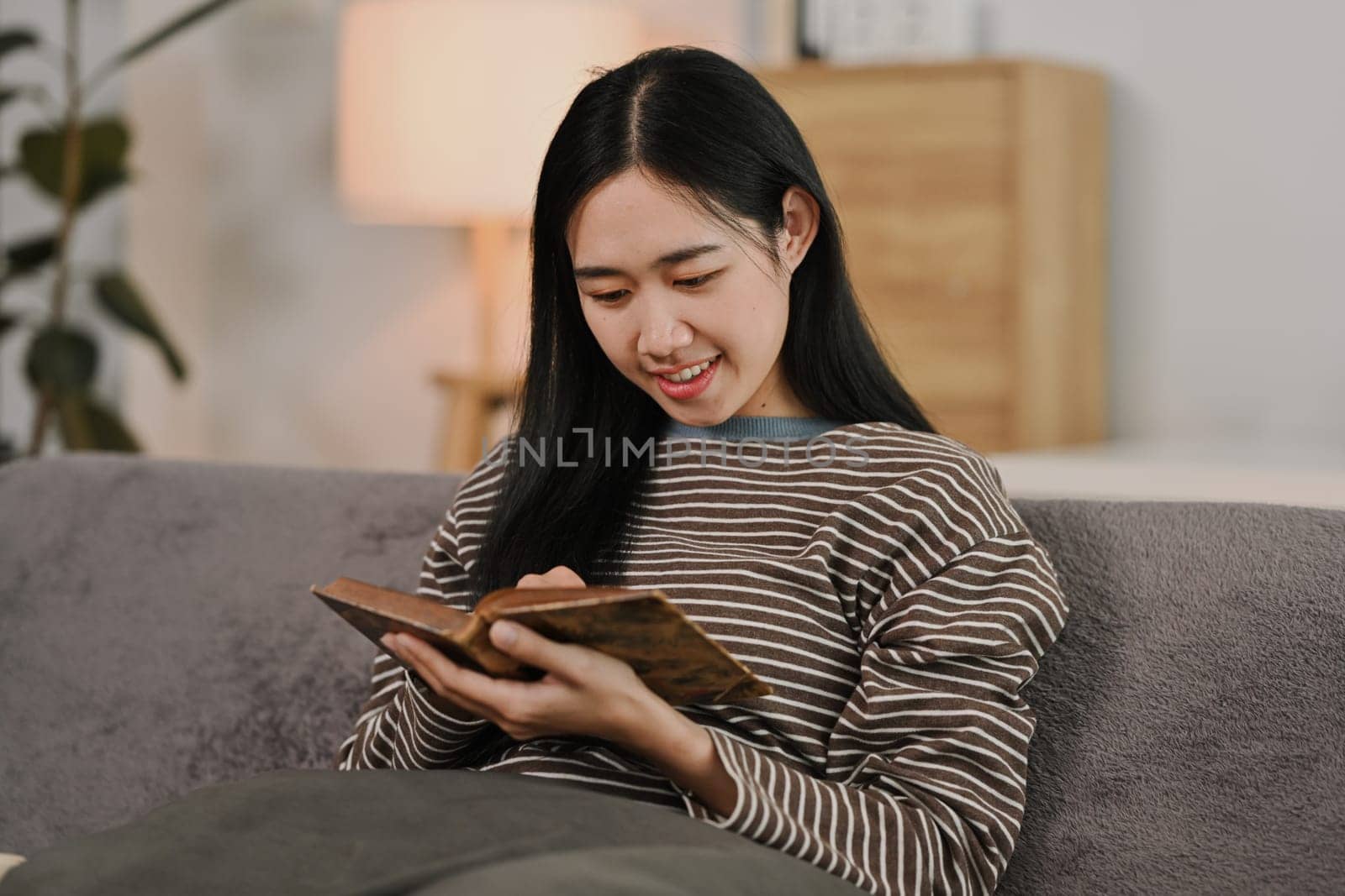 Pretty young woman resting on comfortable couch and reading book. Hobbies, domestic life and lifestyle concept.