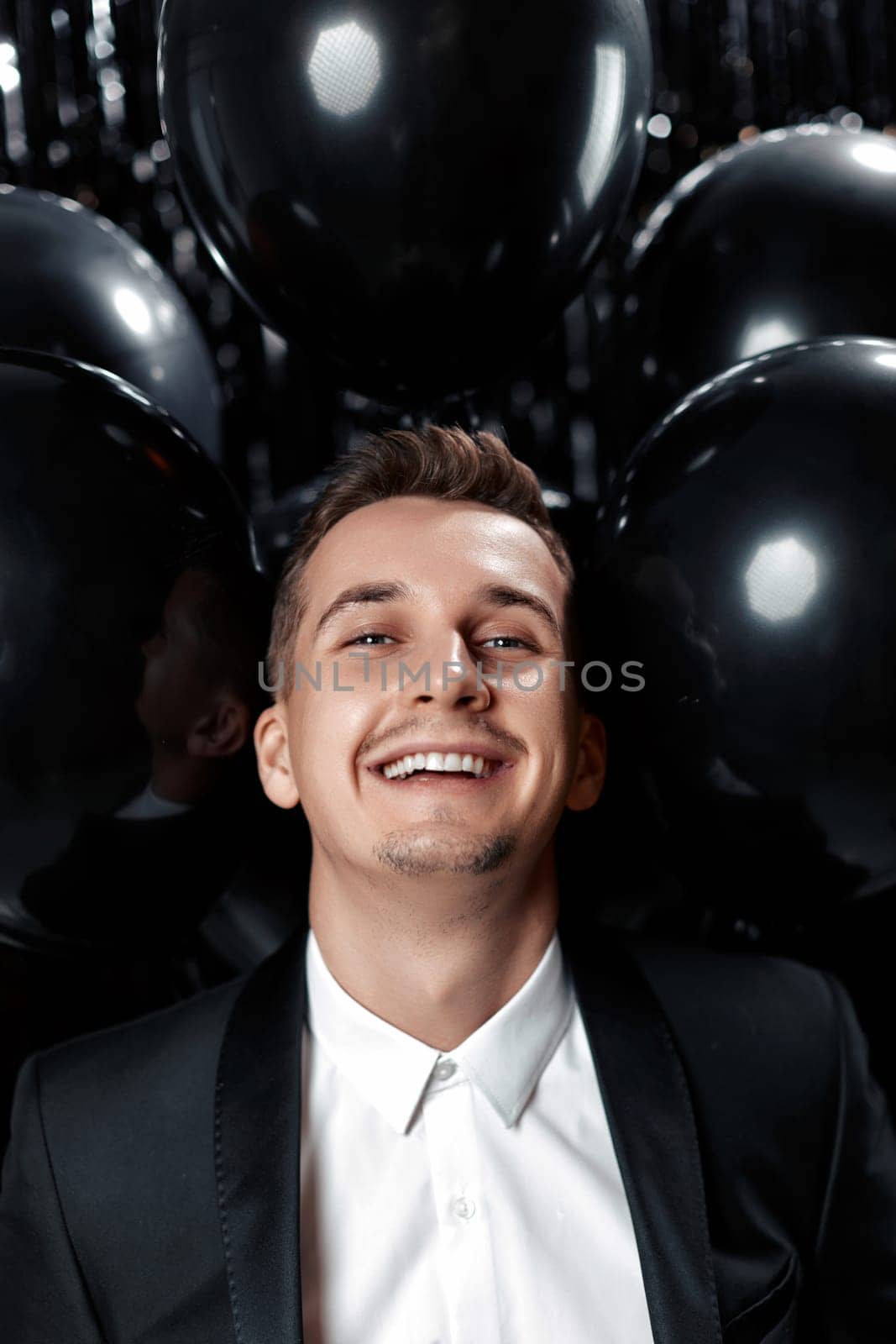 Happy handsome man in black jacket holding black air balloons on glitter background.