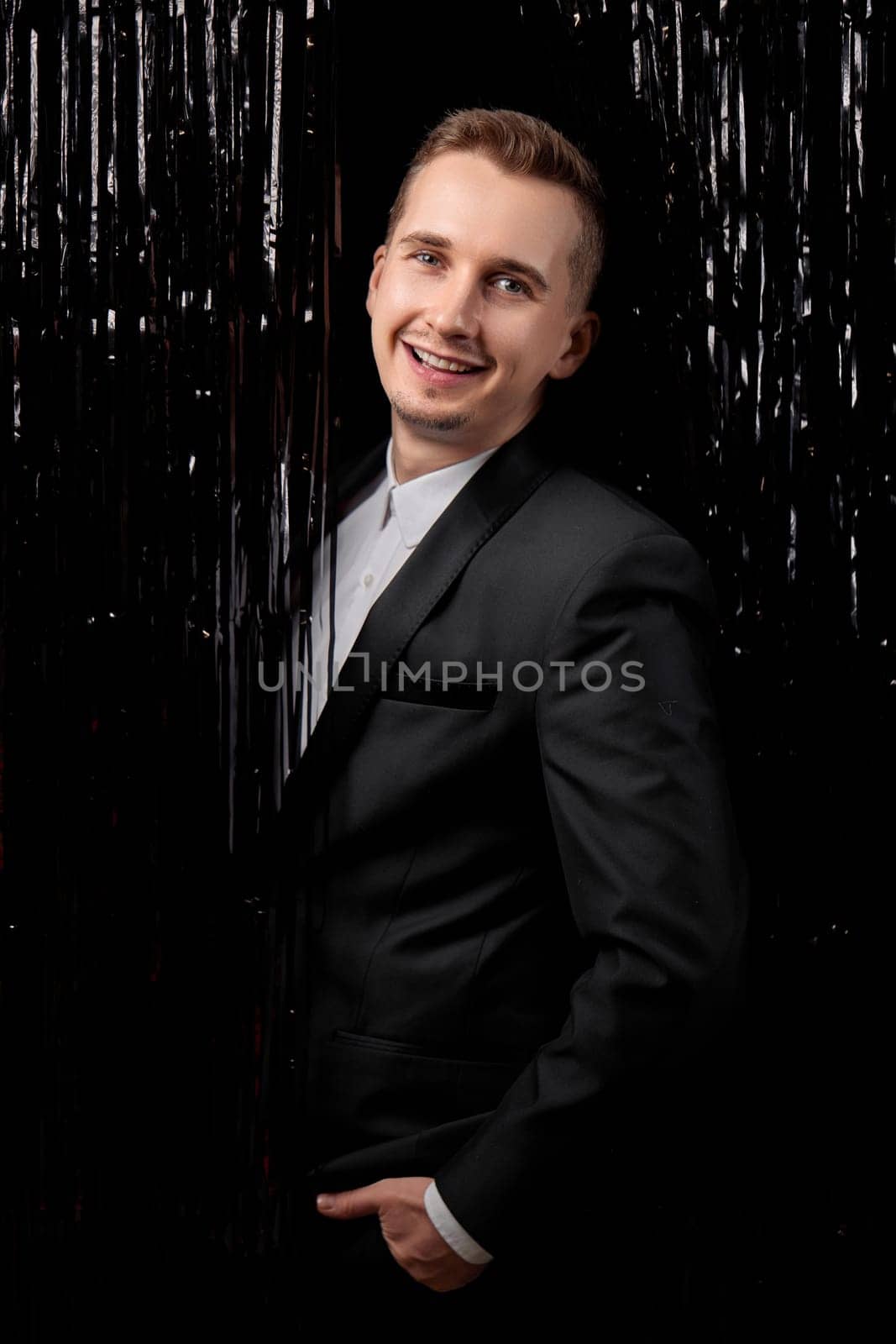 Happy handsome man in black jacket smiling on glitter background.