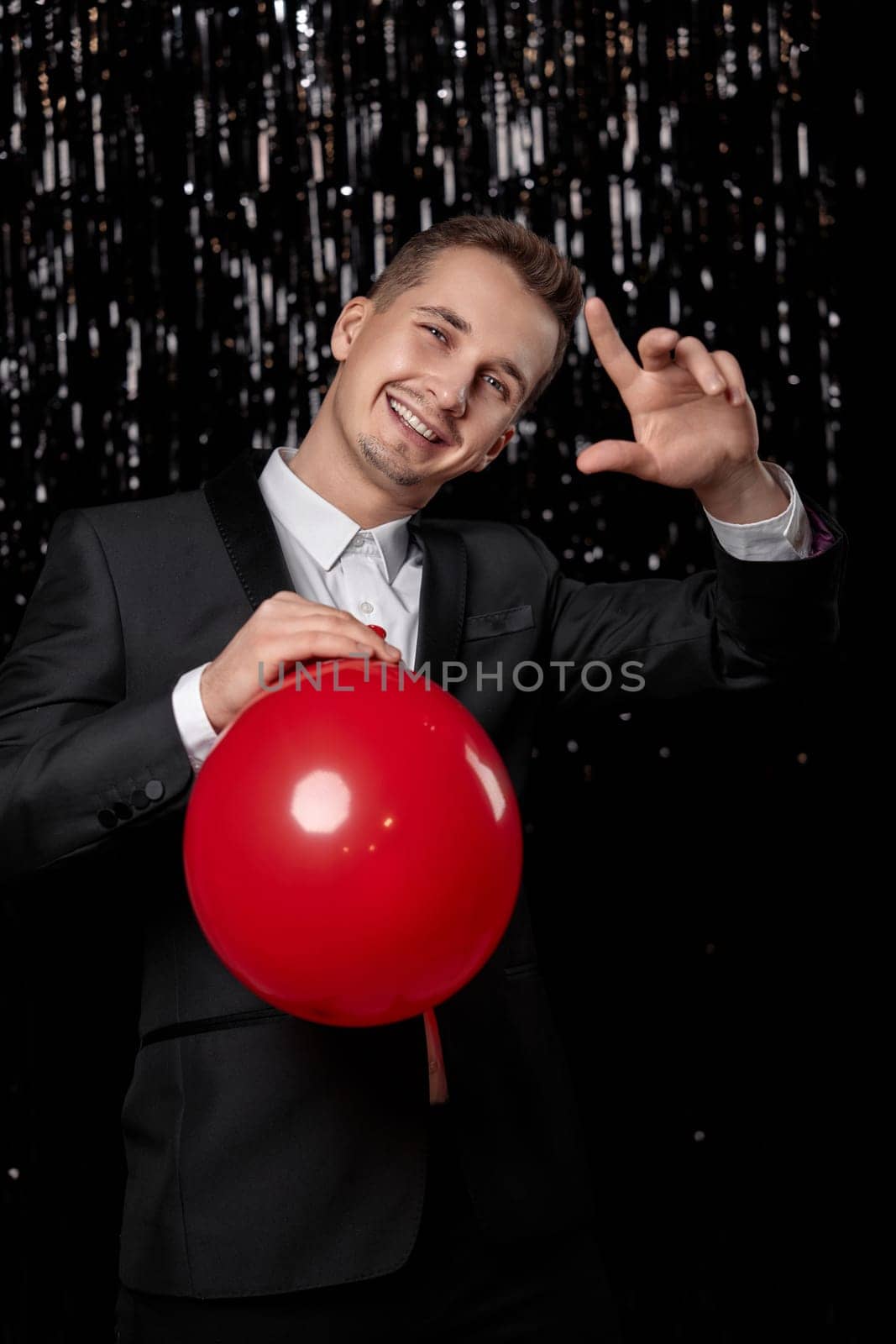 handsome man in black suit with red air balloon on dark glitter background. new year party