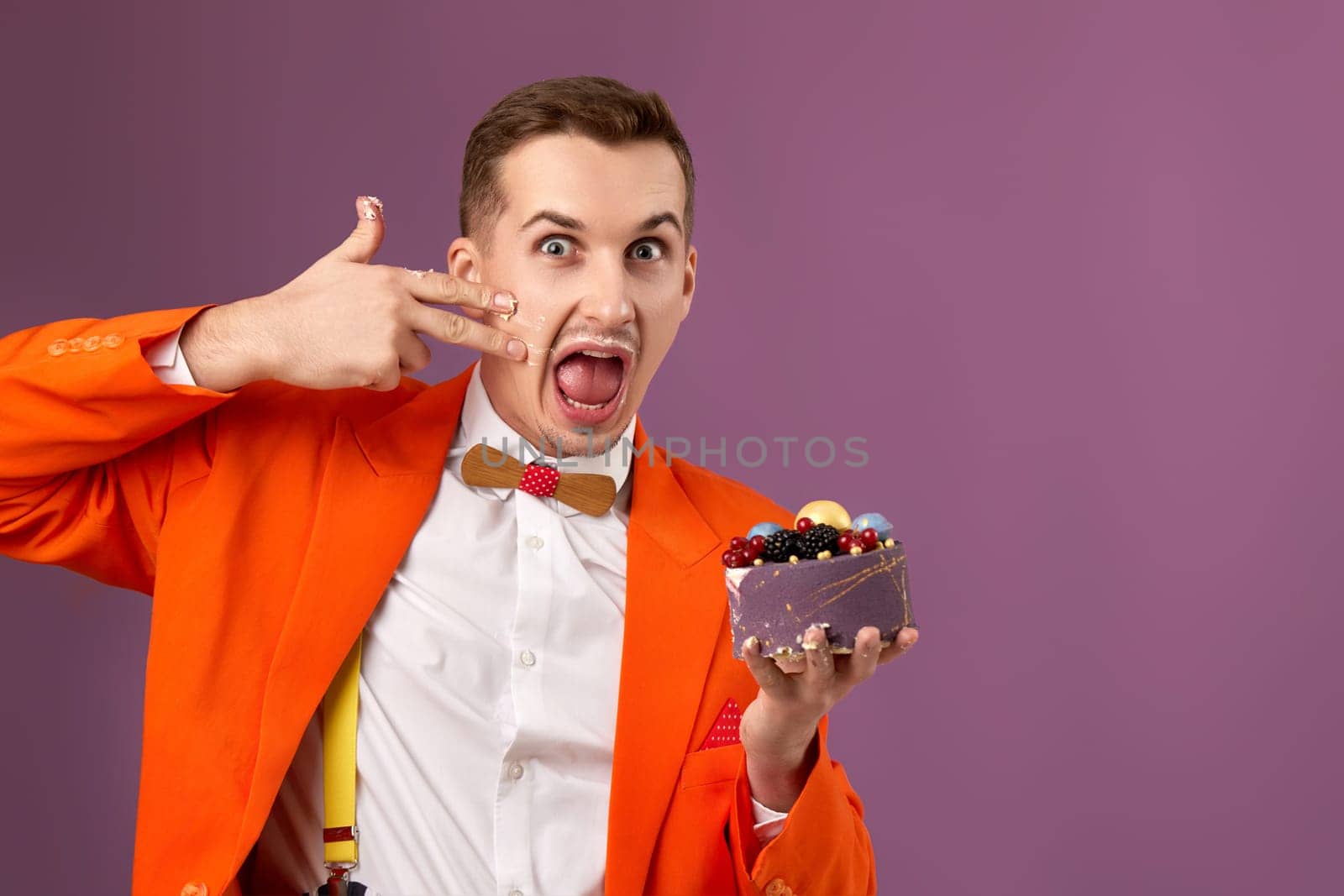 funny man in orange jacket eating cake on purple background