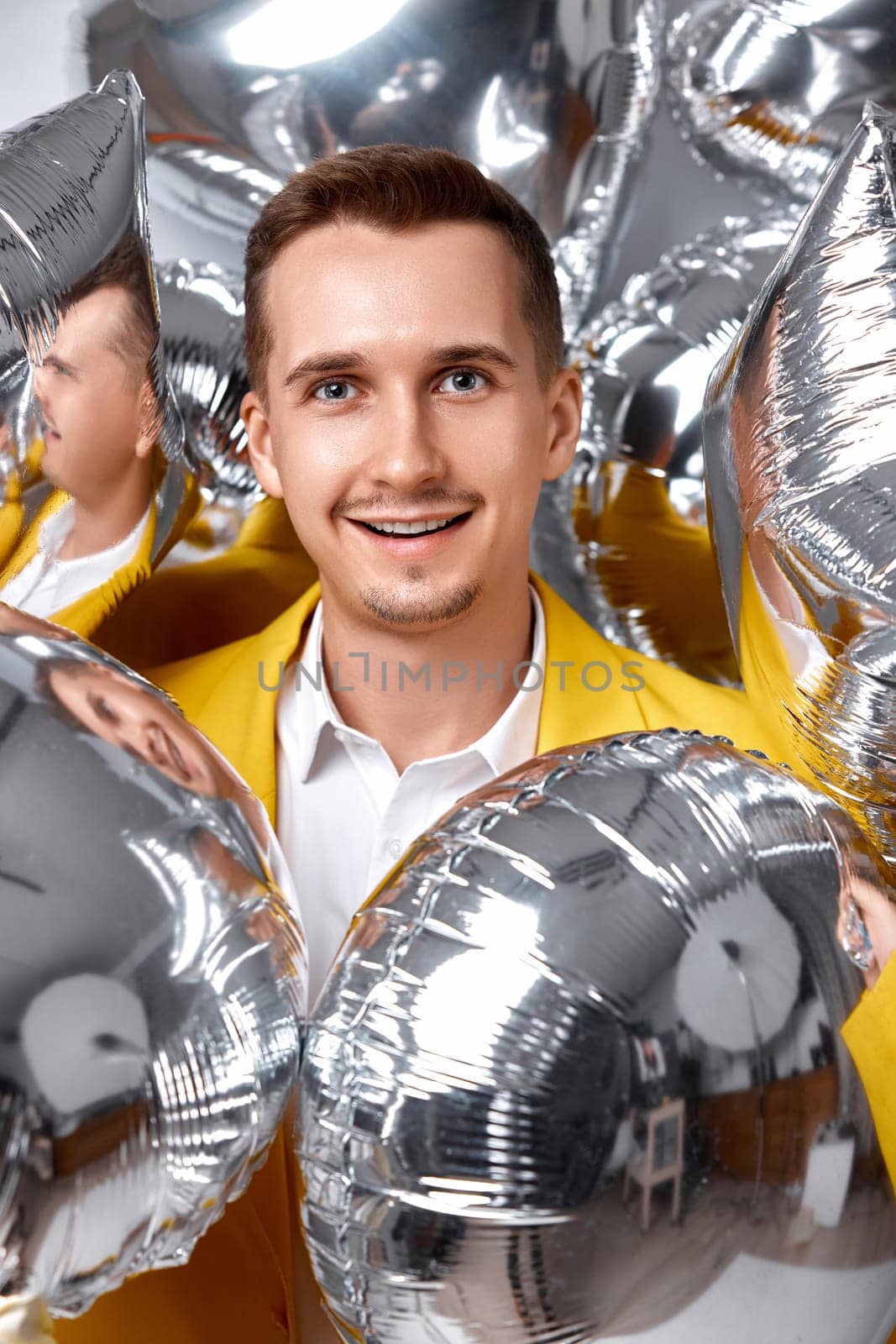 portrait of happy man in yellow jacket with a lot of silver air balloons. birthday party
