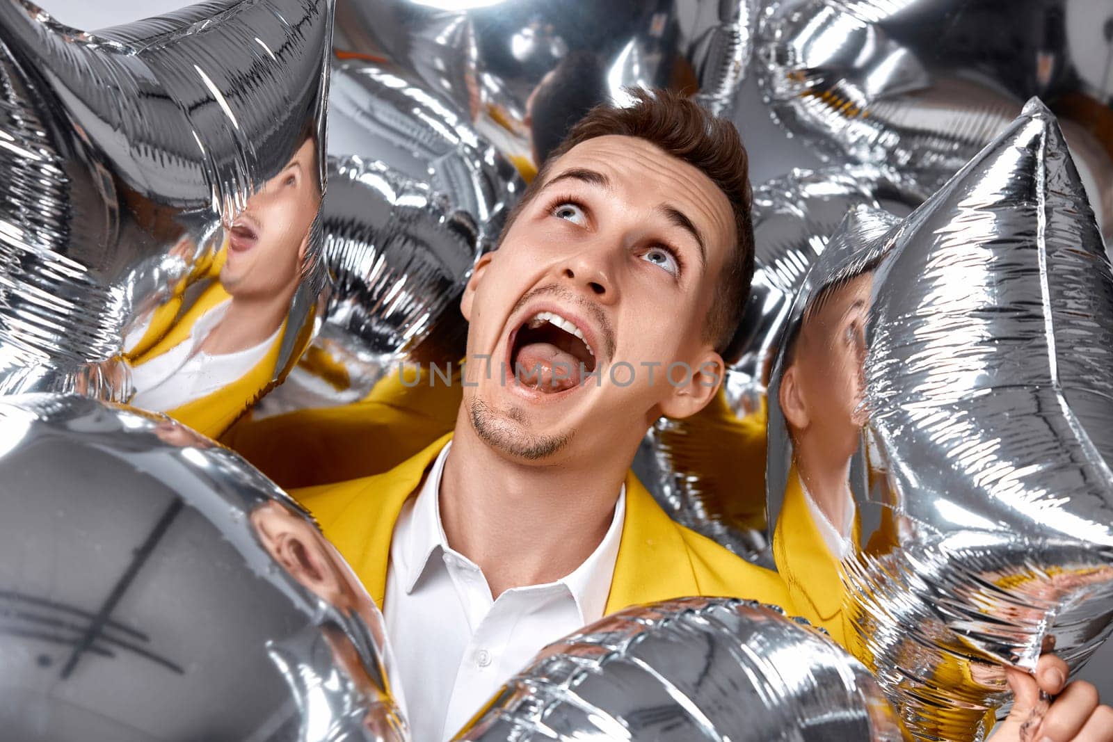 portrait of happy man in yellow jacket with a lot of silver air balloons. birthday party