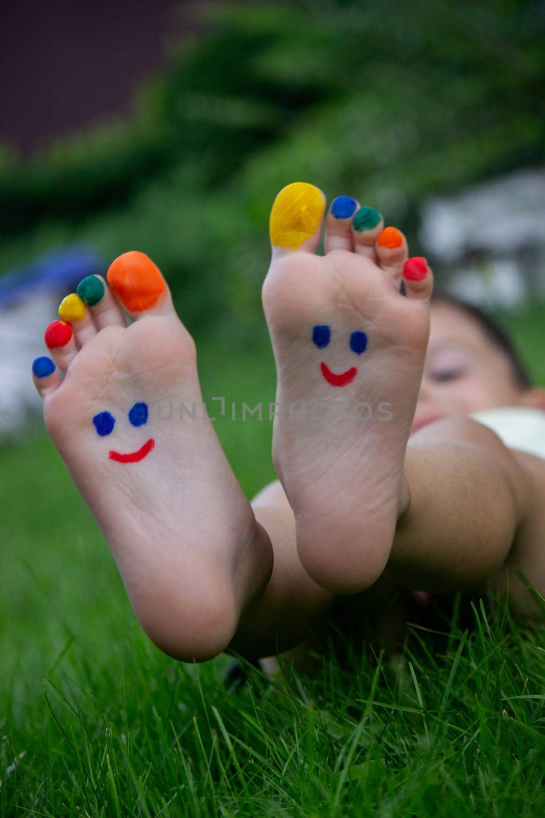 Children's legs with a pattern made of paints are smiling on the green grass.