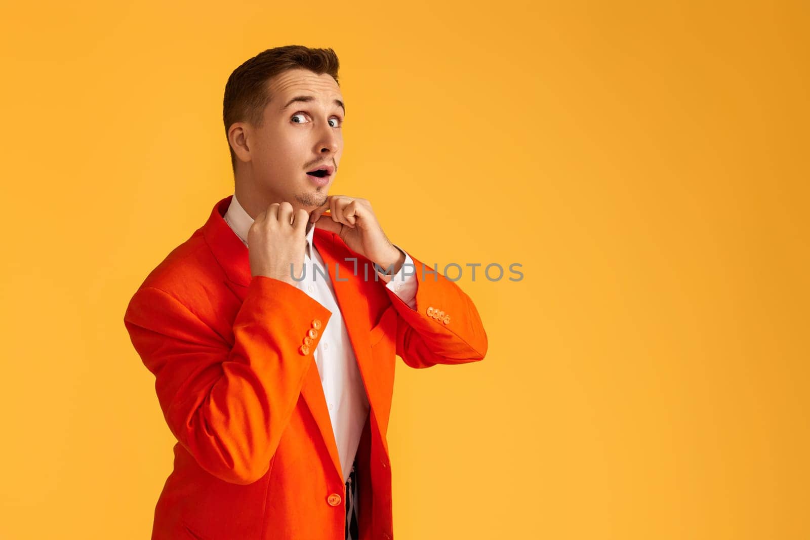 Cheerful extravagant young man in orange jacket on yellow background.