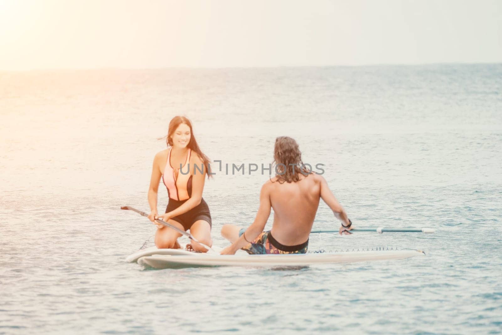 Sea woman and man on sup. Silhouette of happy young woman and man, surfing on SUP board, confident paddling through water surface. Idyllic sunset. Active lifestyle at sea or river