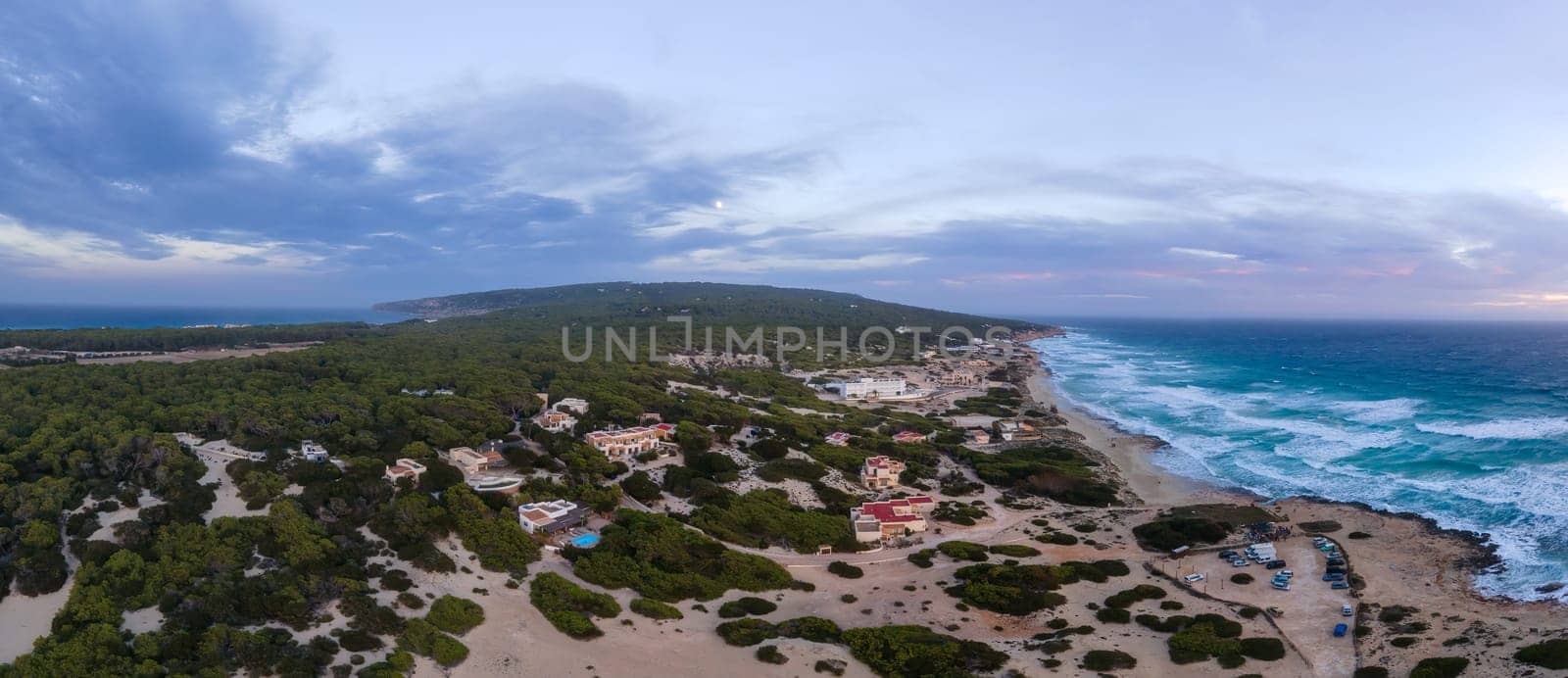 Aerial shot captures a quaint coastal village among nature with a rough sea at twilight.