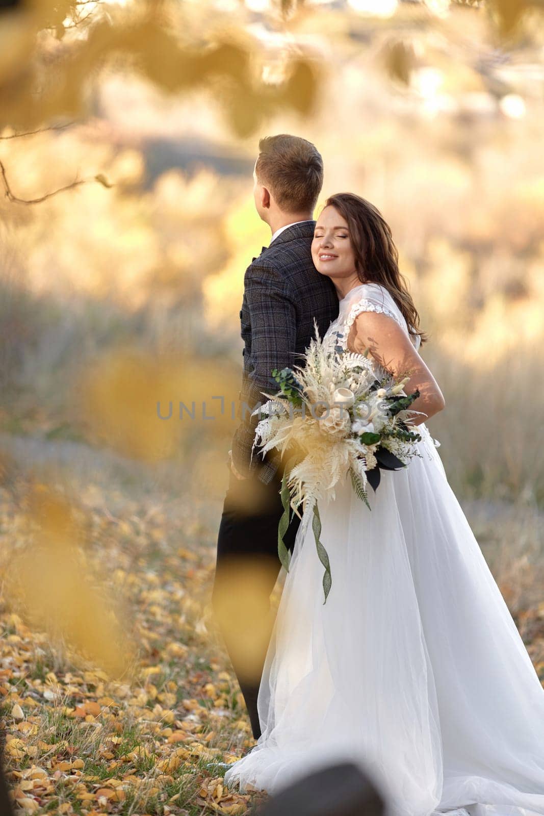beautiful sensual bride in white wedding dress holding bouquet and embracing groom outdoor on natural background