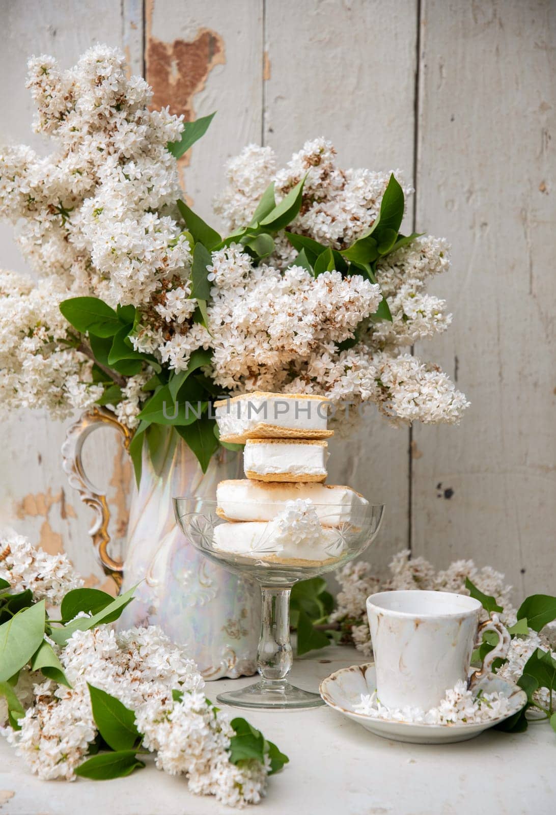 spring still life, a stack of waffle ice cream in a bowl and on a saucer, with a bouquet of white lilacs in tea pot by KaterinaDalemans