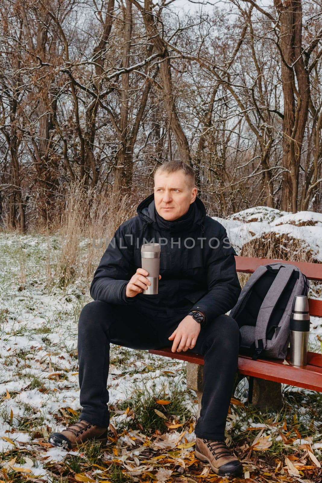 Winter Serenity: 40-Year-Old Man Enjoying Tea on Snow-Covered Bench in Rural Park. Immerse yourself in the tranquil beauty of winter as a 40-year-old man finds solace on a snowy bench in a rural park. by Andrii_Ko