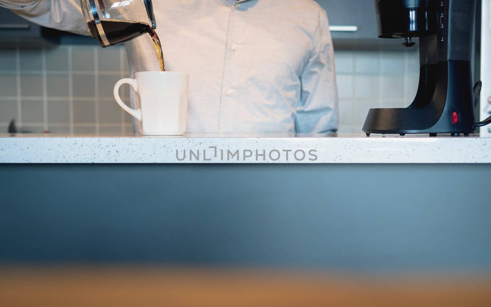 Man in the kitchen pouring a mug of hot filtered coffee from a glass pot in the morning