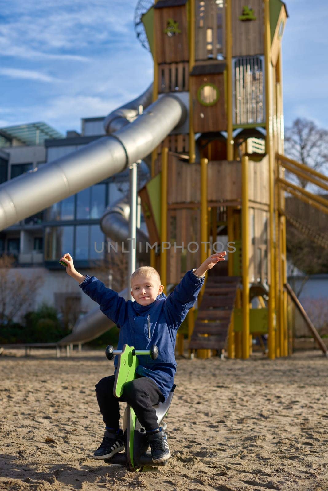 Childhood Joy: Beautiful 8-Year-Old Boy in Jacket Swinging on Horse-Shaped Seesaw, Background of Playful Park in Bietigheim-Bissingen, Germany, Autumn by Andrii_Ko