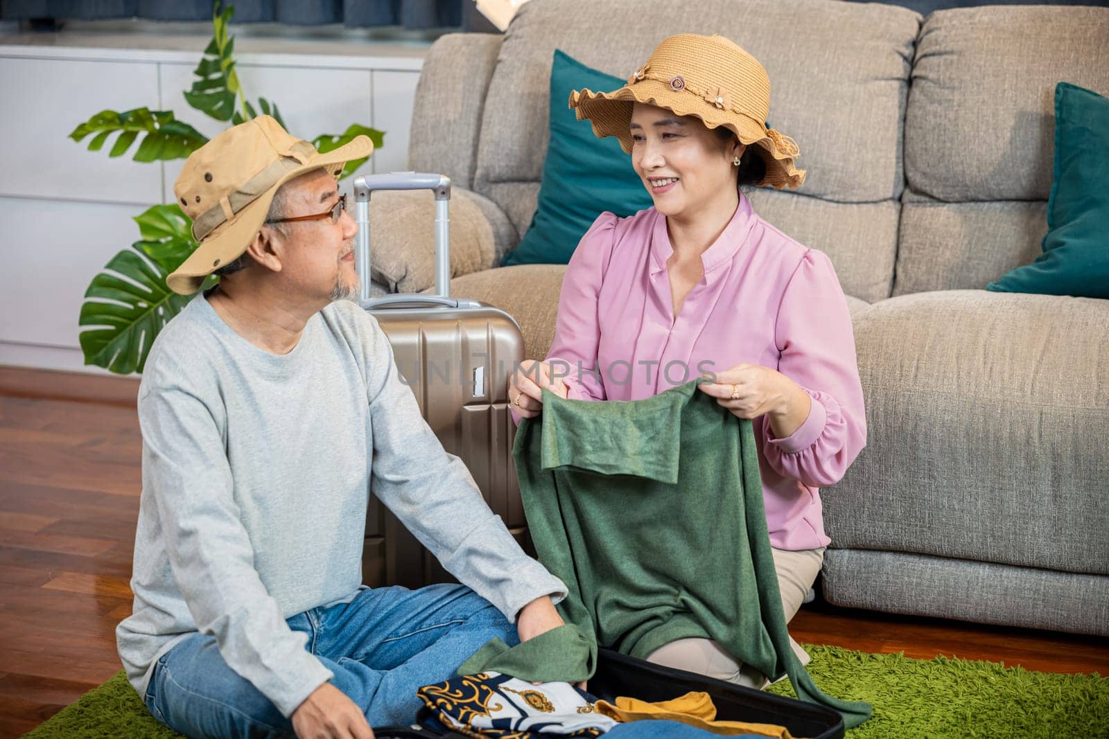Asian couple old senior marry retired couple prepare luggage suitcase arranging for travel, Romantic retired packing clothes travel bag suitcase together on floor at home interior living room