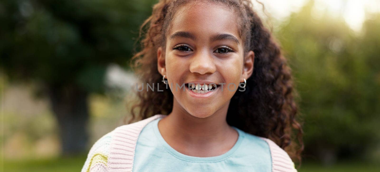 Face, child or girl laughing outdoor in a garden, park or green environment for fun and happiness. Portrait of a young African female kid with a positive mindset, cute smile and nature to relax.