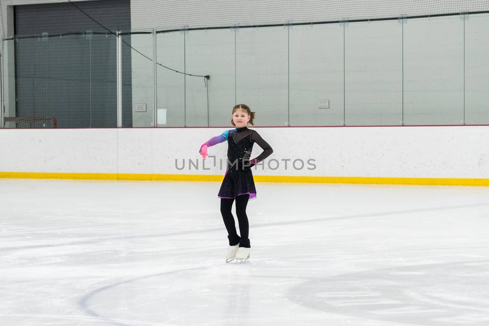 Young girl perfecting her figure skating routine while wearing her competition dress at an indoor ice rink.