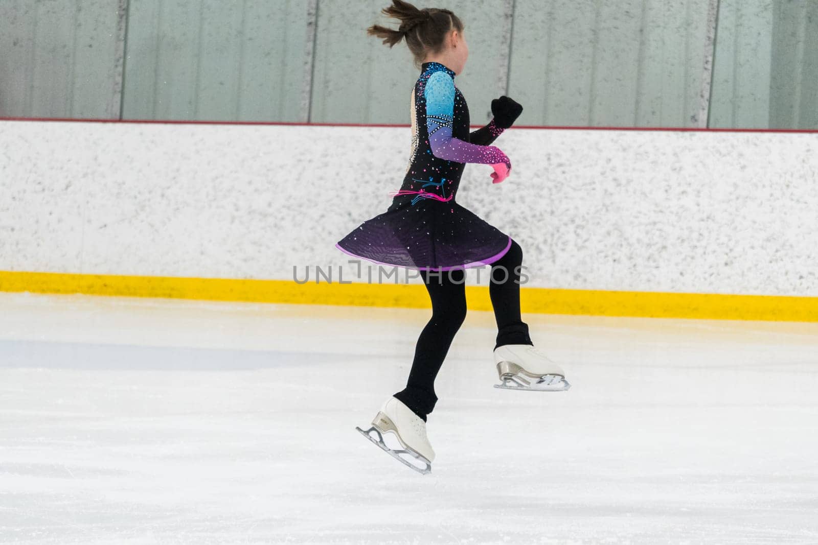 Young girl perfecting her figure skating routine while wearing her competition dress at an indoor ice rink.