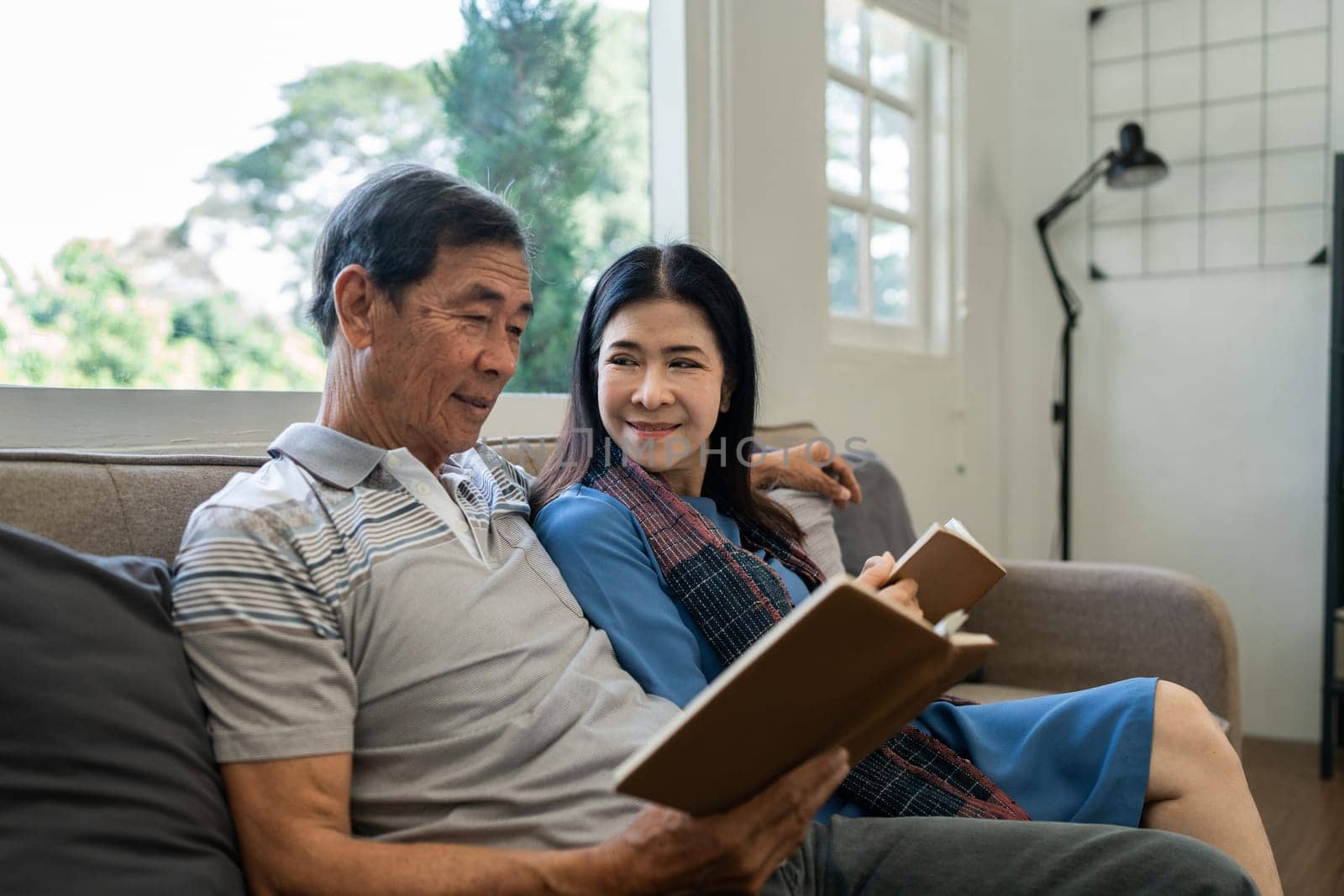 Retired elderly couple sits on couch in their home reading relaxing book. Senior Activity Concept.