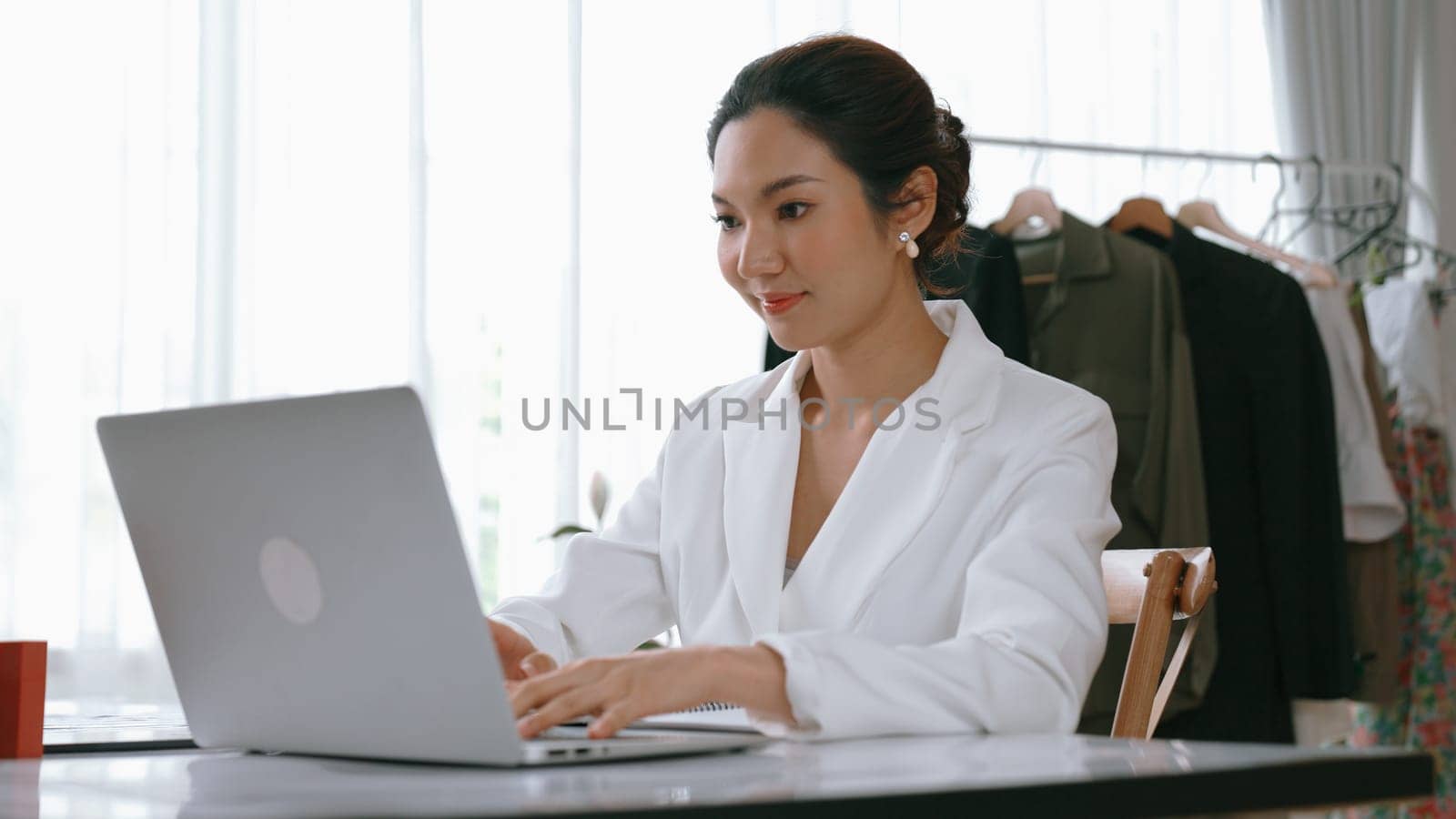 Young businesswoman sitting on the workspace desk using laptop computer for internet online content writing or remote working from home. Clothing and textile business marketing analysis. Vivancy