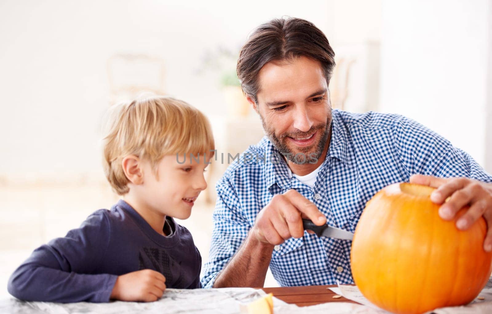 Father, child and carving pumpkin with knife to celebrate halloween, fun craft and creativity at home. Happy boy kid, dad and family cutting orange vegetable for holiday lantern, party and decoration by YuriArcurs