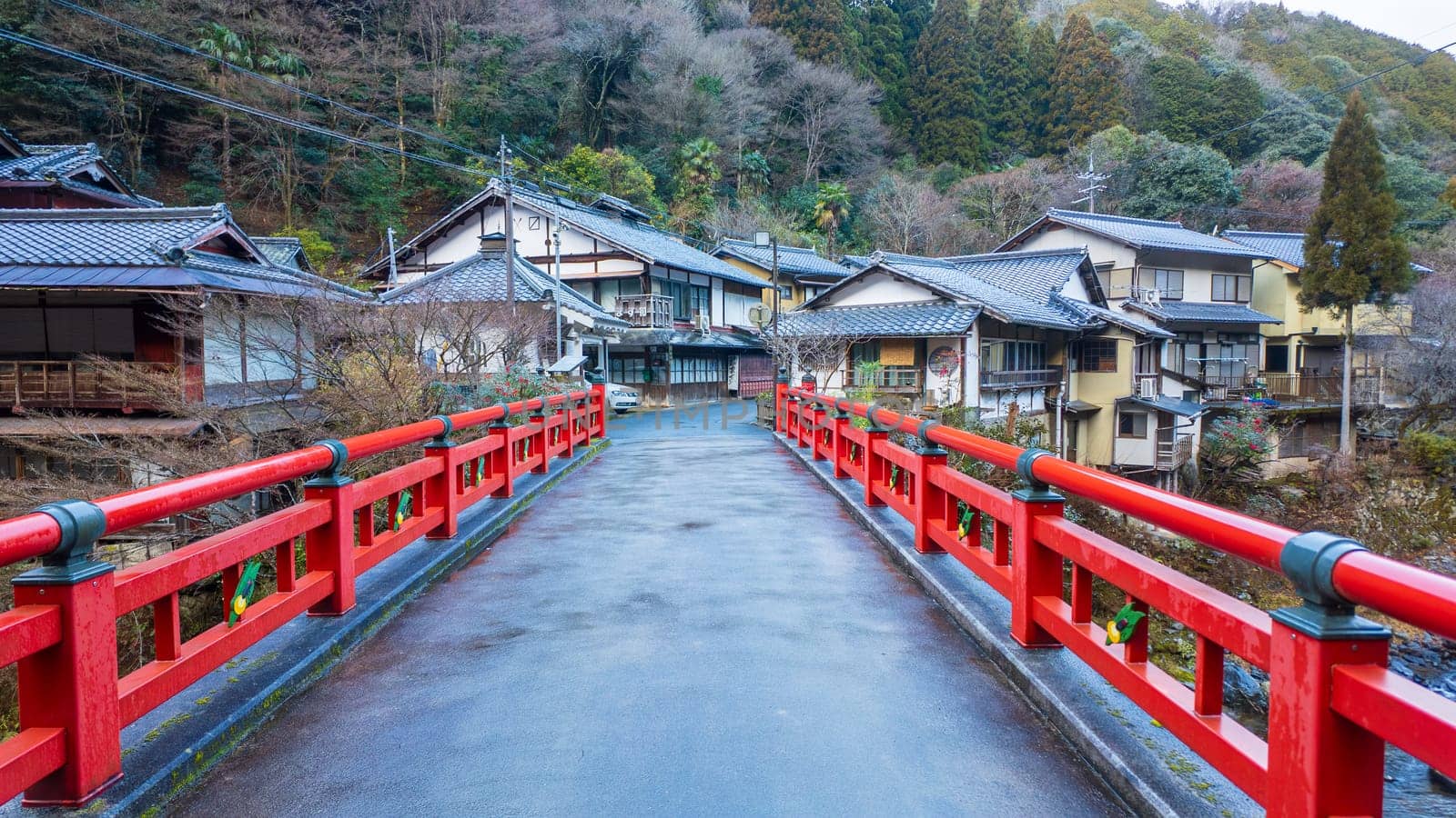 Narrow red bridge leads to traditional houses in Japanese village by Osaze