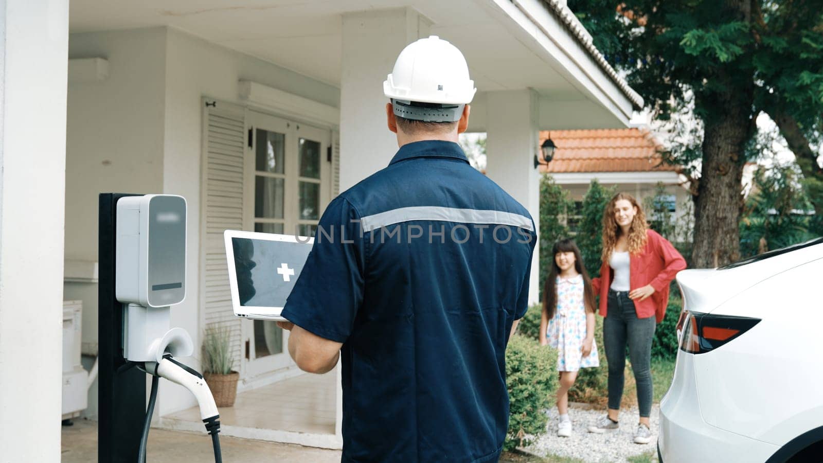 Qualified technician working on home EV charging station installation, making troubleshooting and configuration setup on charging system with empty laptop screem for EV at home. Synchronos