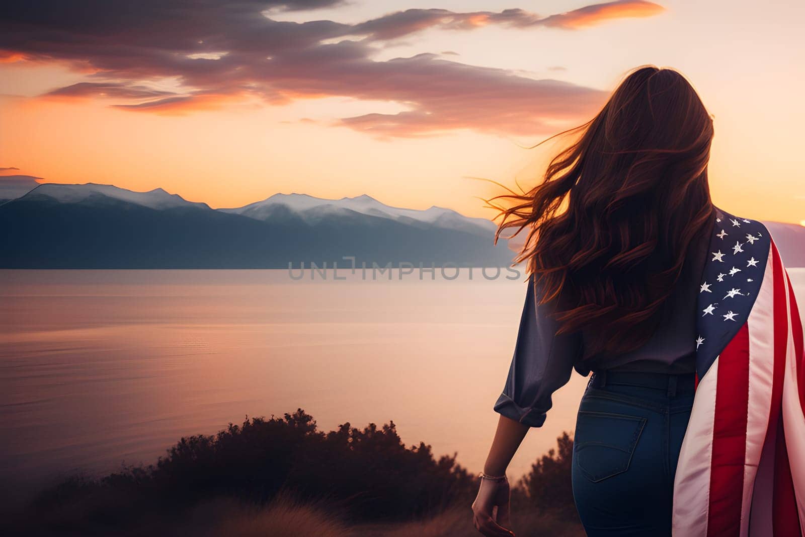 Rear view of a young woman with long hair with a USA flag on her shoulders enjoying the sunset in nature.