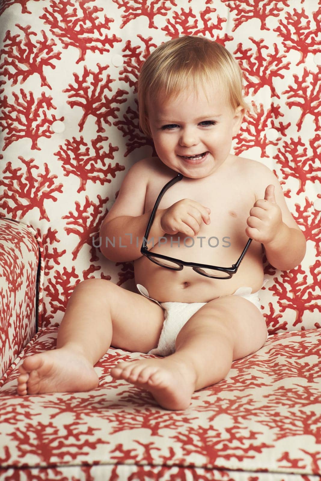 Happy, glasses and funny baby in studio with vision, eye care and health for child development. Smile, excited and young infant, toddler or kid play with spectacles or eyewear by wallpaper background.