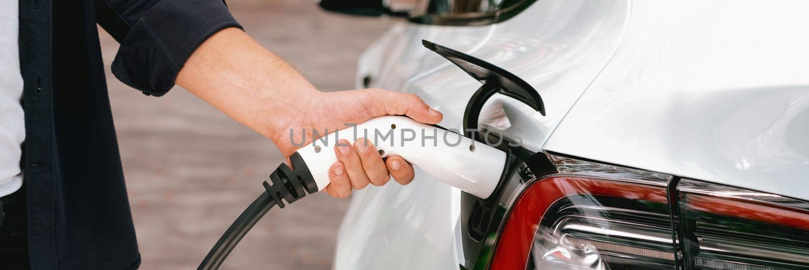 Panorama banner man recharging battery for electric car during autumnal road trip travel EV car in autumnal forest. Eco friendly travel on vacation during autumn with electric vehicle. Exalt