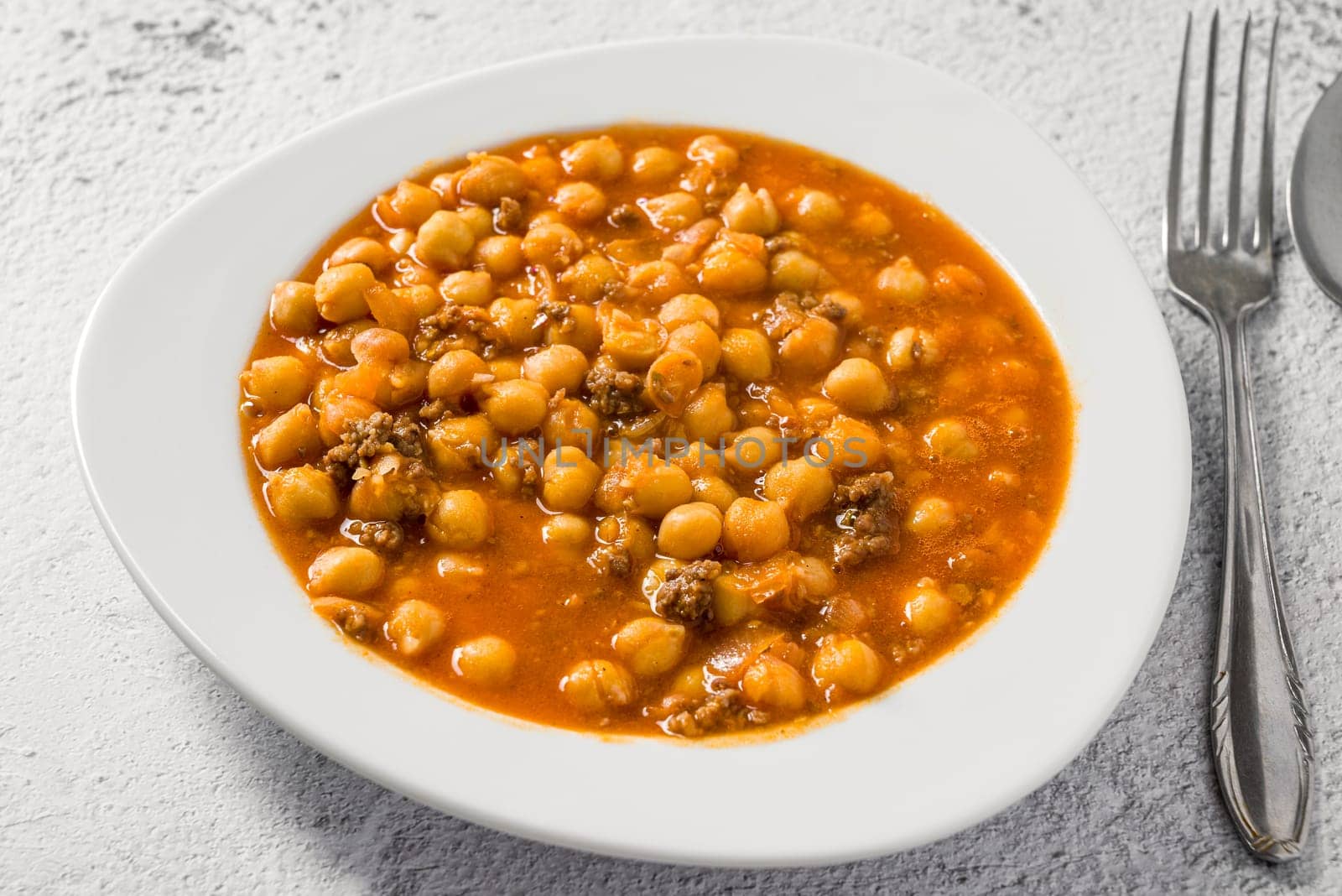 Chickpea stew with minced meat on a white porcelain plate on a stone table by Sonat