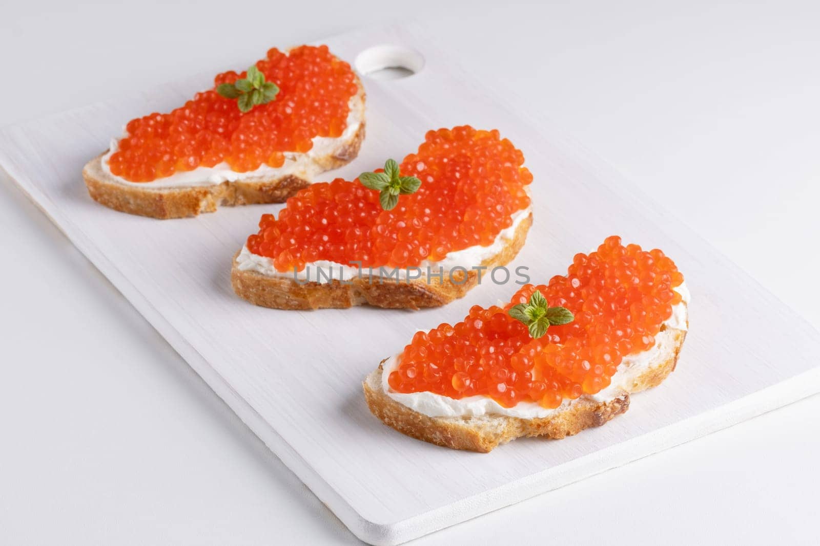Three sandwiches with red caviar on a cutting board. A delicious appetizer of trout caviar on a slice of bread with cream cheese. Salted salmon caviar for fish delicacy concept.