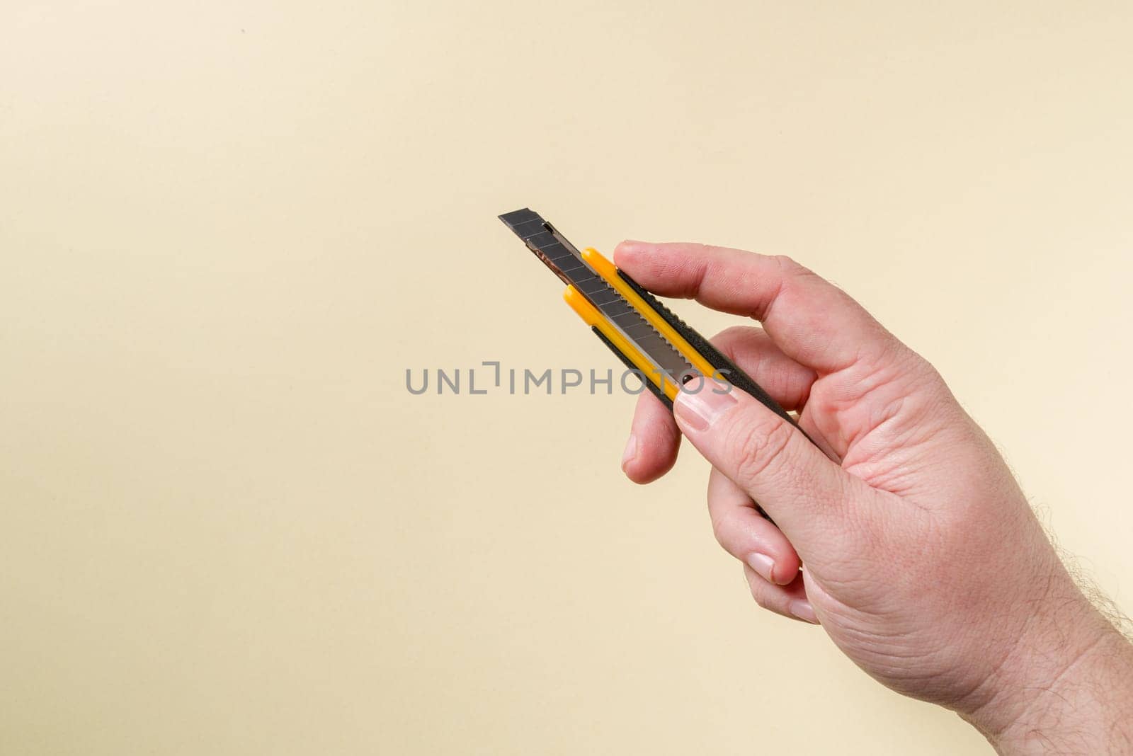 Hand holding a yellow and black metal utility knife in front of a yellow background