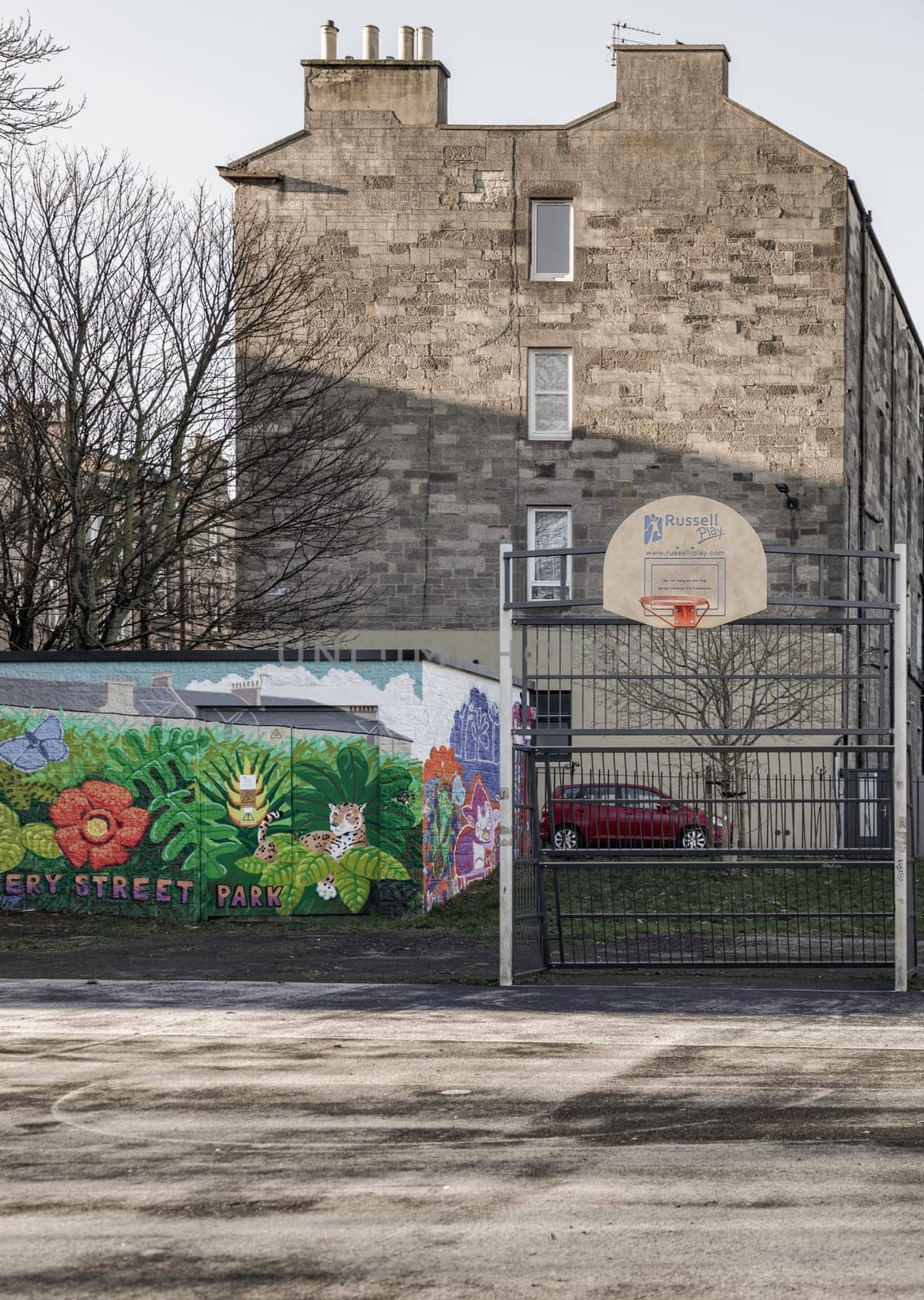 Edinburgh, Scotland, Jan 17, 2024 - Basketball backboard with the orange hoop metal ring at outdoor basketball courts in the park against old buildings background in the city downtown. Space for text, Selective focus.